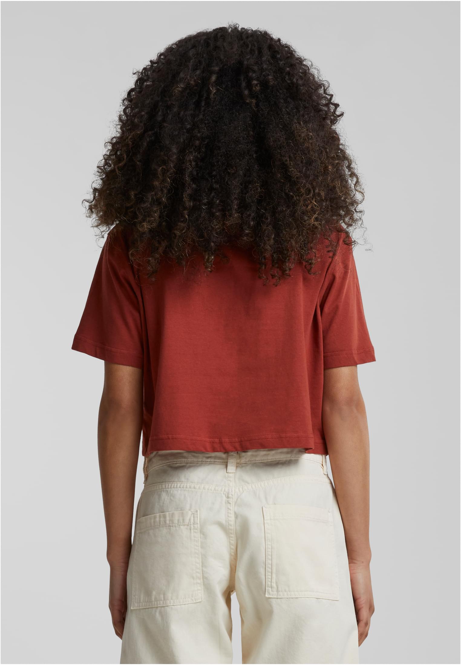 Kvinna sedd bakifrån, klädd i en terrakottafärgad Ladies Short Oversized Tee och ett par ljusa byxor.