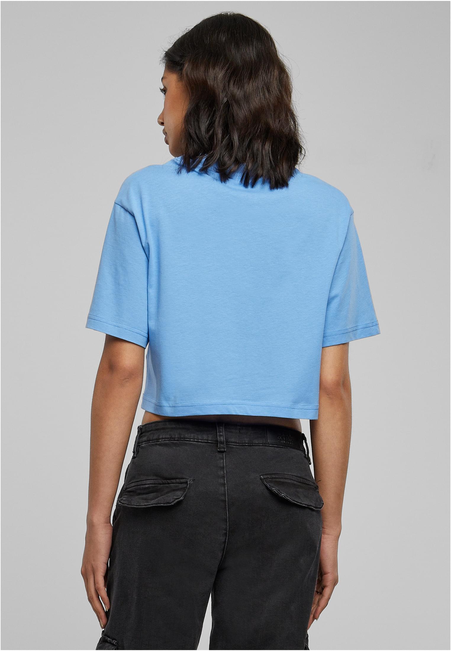 Kvinna sedd bakifrån, iklädd en ljusblå, kort, oversized t-shirt och svarta byxor.