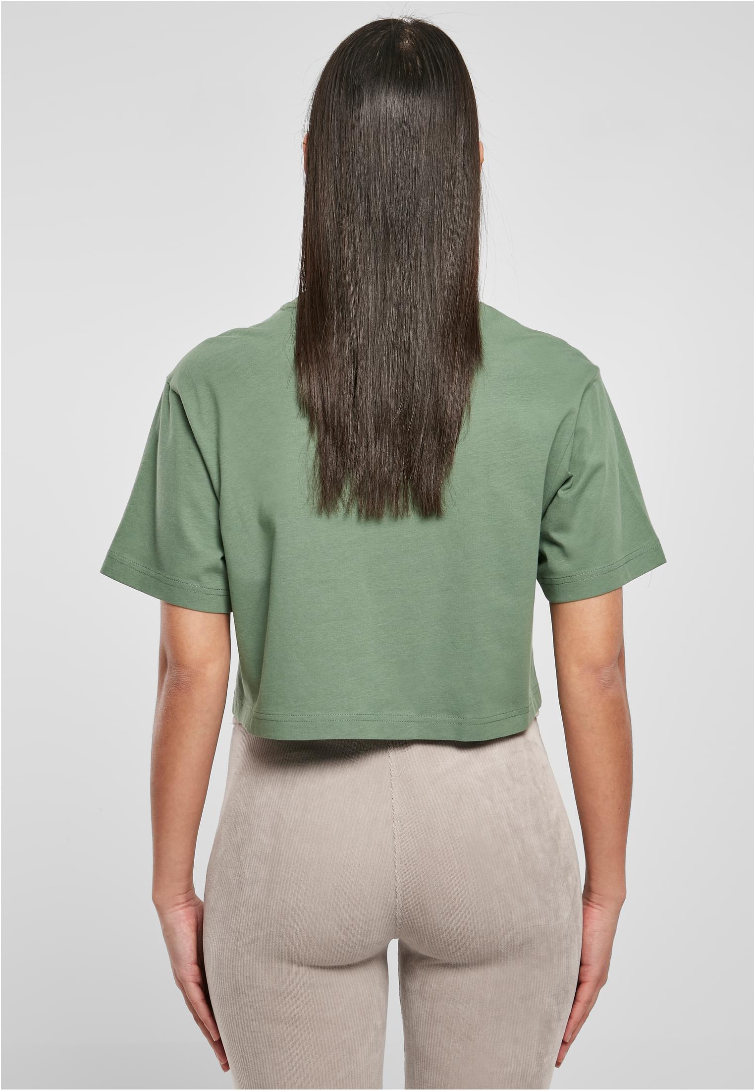 Baksidan av en kvinna som bär en grön, kort, oversized t-shirt och beiga, ribbade leggings.