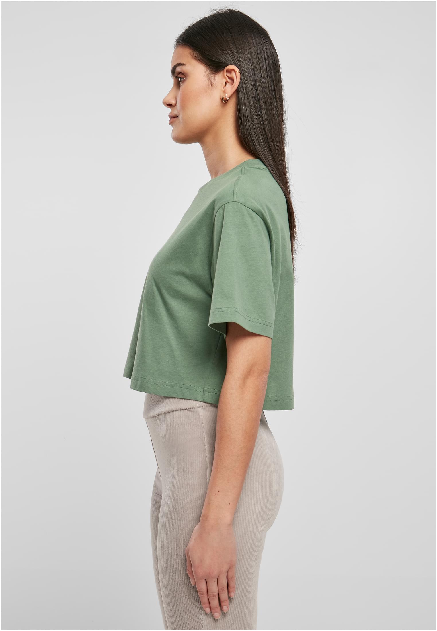 Sidovy av en kvinna som bär UC Ladies Short Oversized Tee i grönt, tillsammans med ljusbeiga manchesterbyxor.