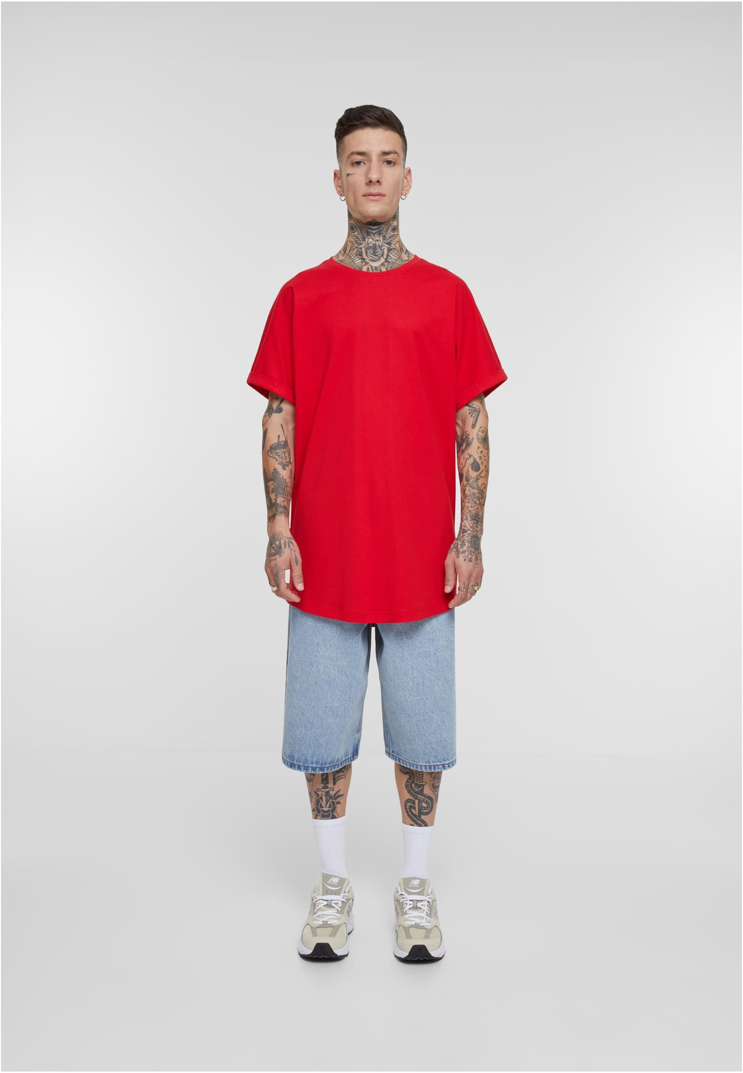 Manlig modell sedd framifrån, klädd i en röd Long Shaped Turnup Tee, jeansshorts och sneakers.