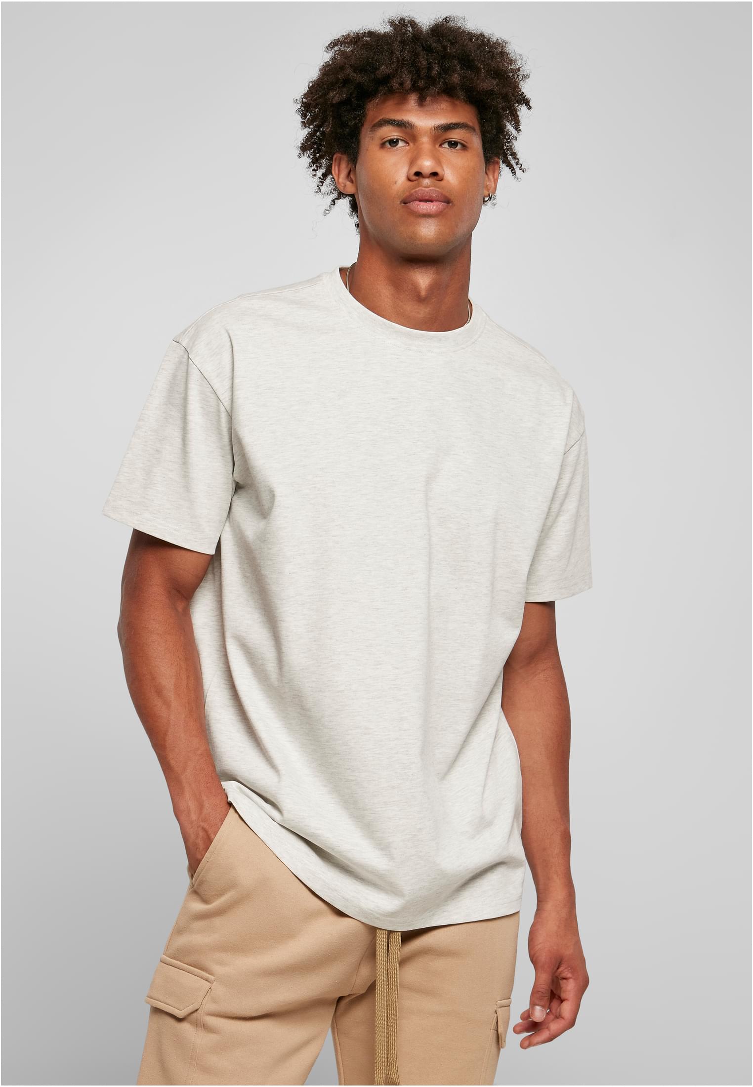 En manlig modell poserar i en ljusgråmelerad Heavy Oversized Tee och beige byxor mot en ljusgrå bakgrund.