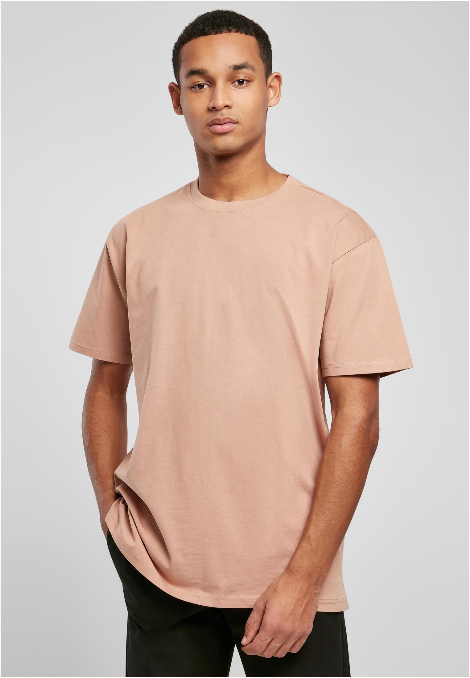 Manlig modell som bär en ljusrosa, oversized t-shirt från Urban Classics och svarta byxor.