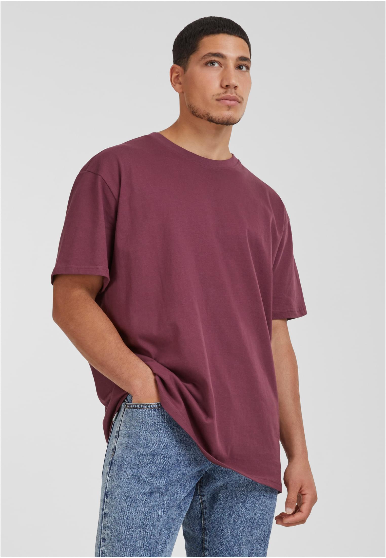 Manlig modell som bär en vinröd UC Heavy Oversized Tee och blå jeans.