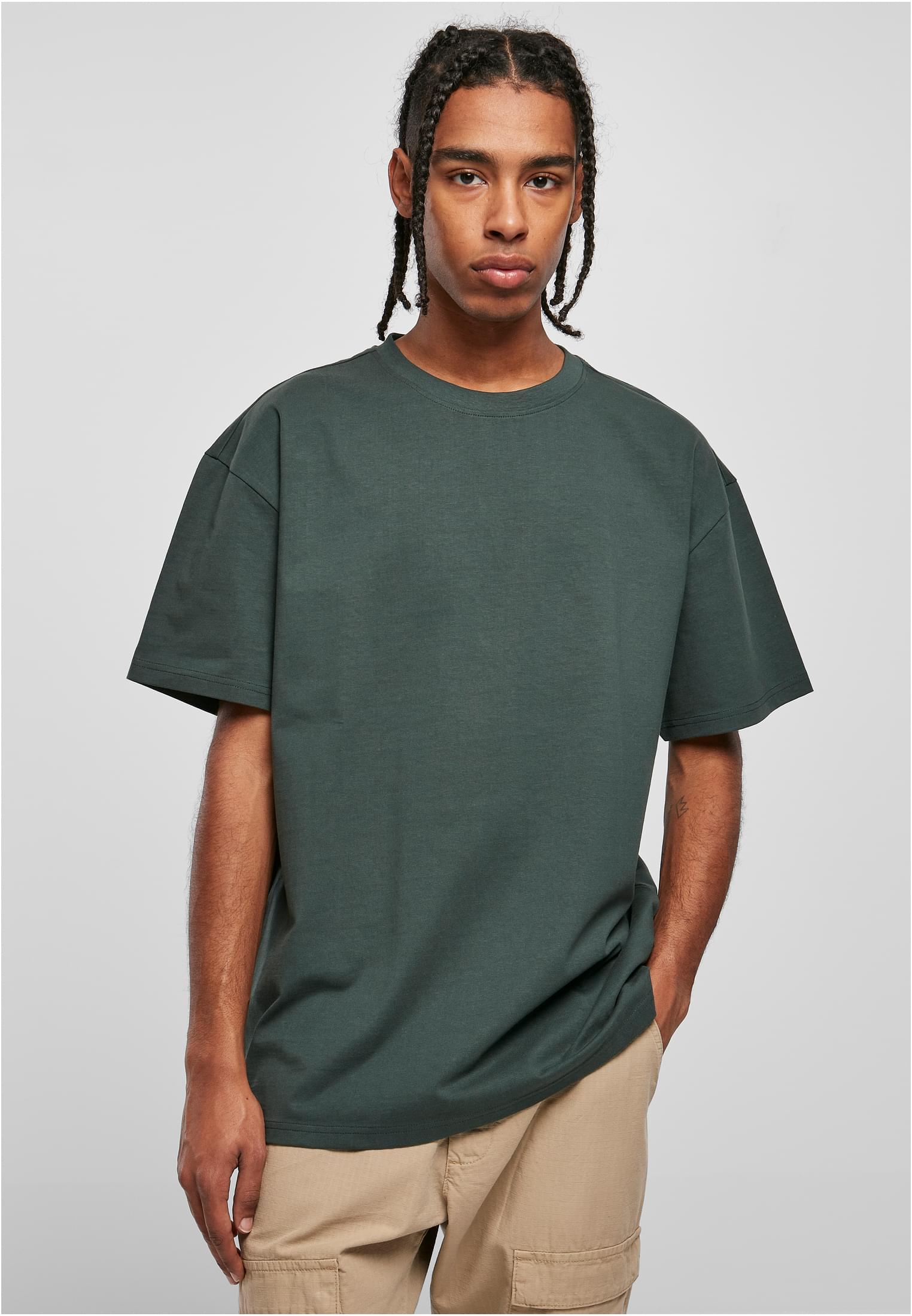 En manlig modell med flätor som bär en mörkgrön Heavy Oversized T-shirt och beiga byxor.