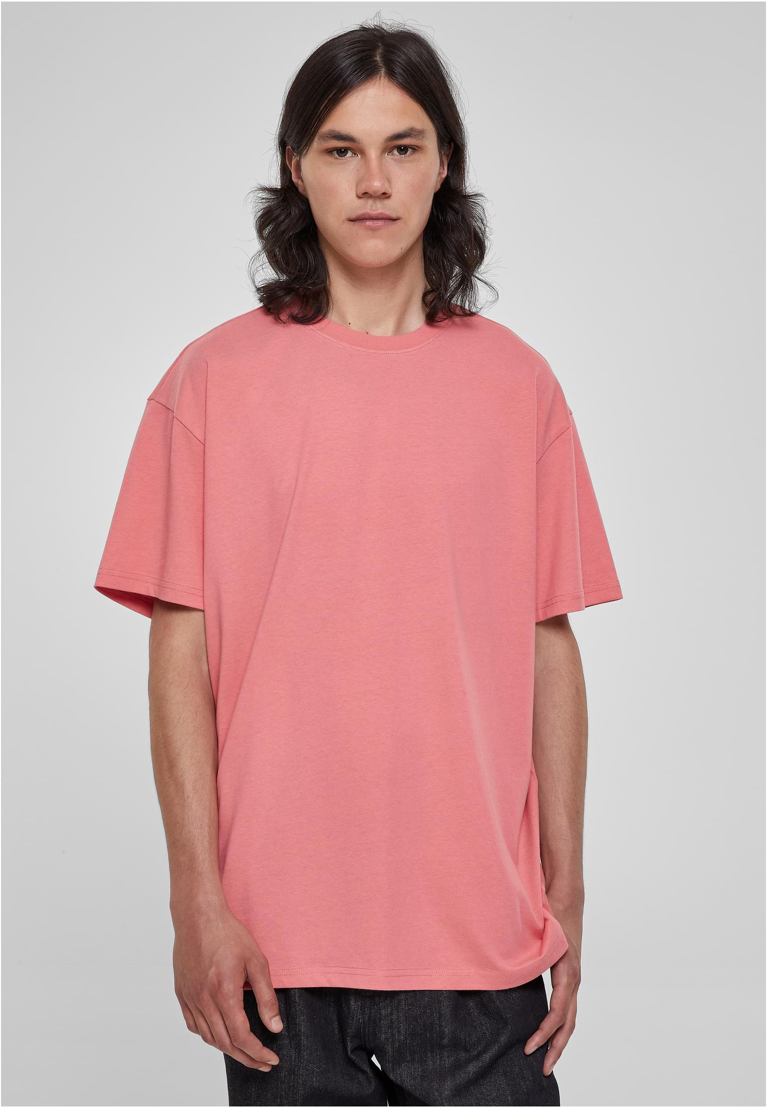 Manlig modell med långt, mörkt hår som bär en laxrosa Heavy Oversized T-shirt från Urban Classics.