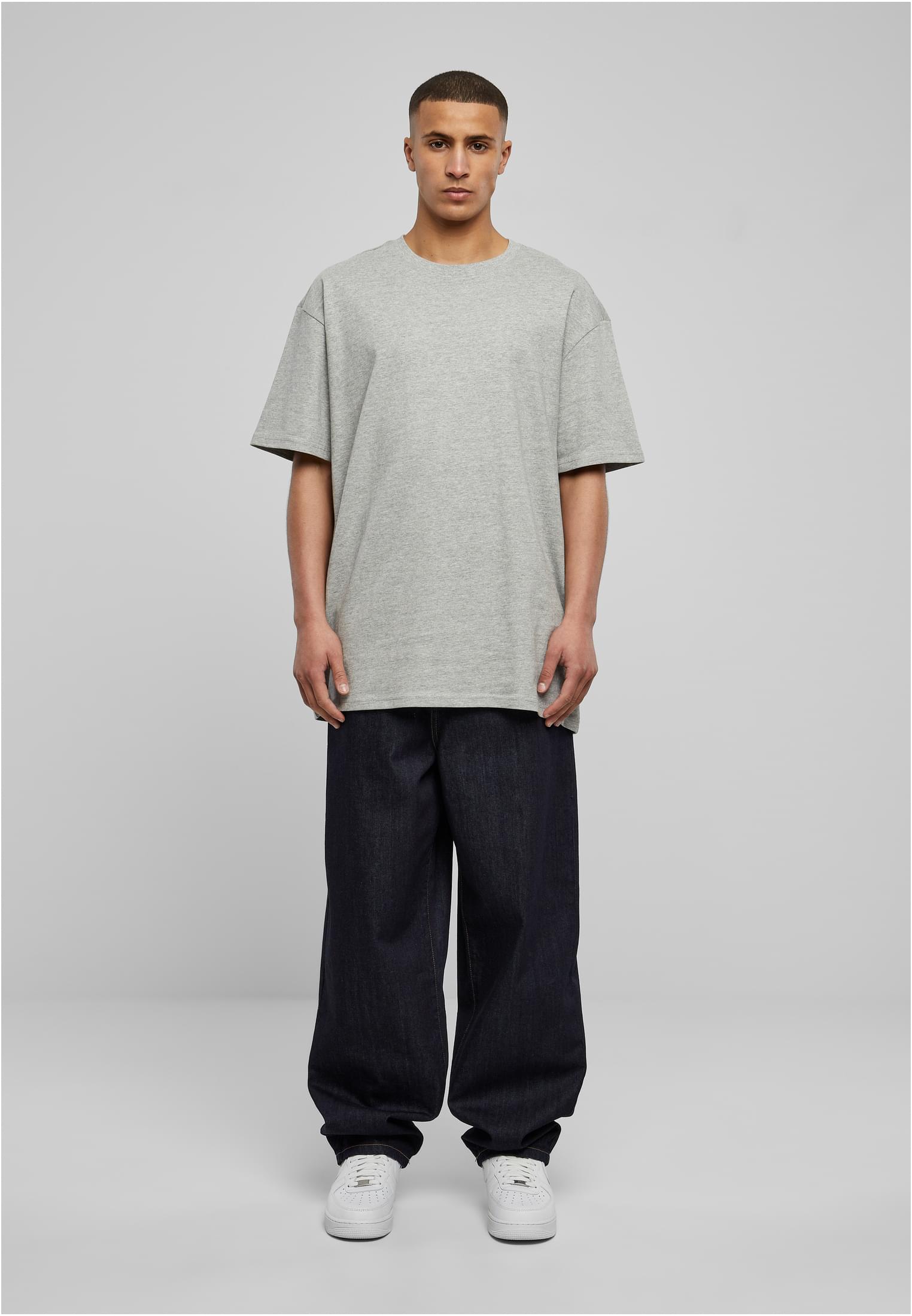 Frontbild på en manlig modell klädd i en grå oversized t-shirt, mörka vida jeans och vita sneakers.