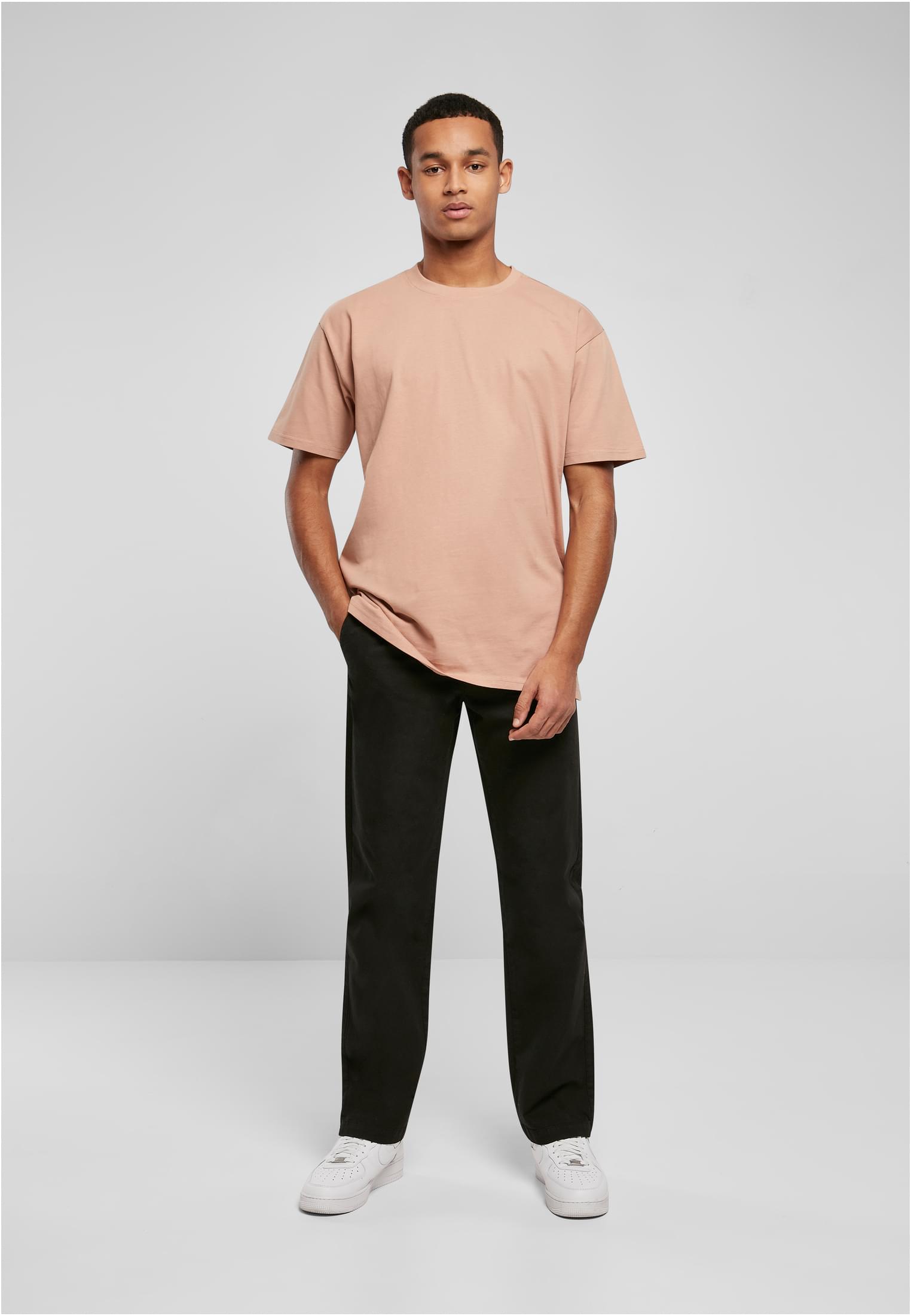 Manlig modell som bär en ljus, oversize t-shirt, svarta byxor och vita sneakers mot en ljusgrå bakgrund.