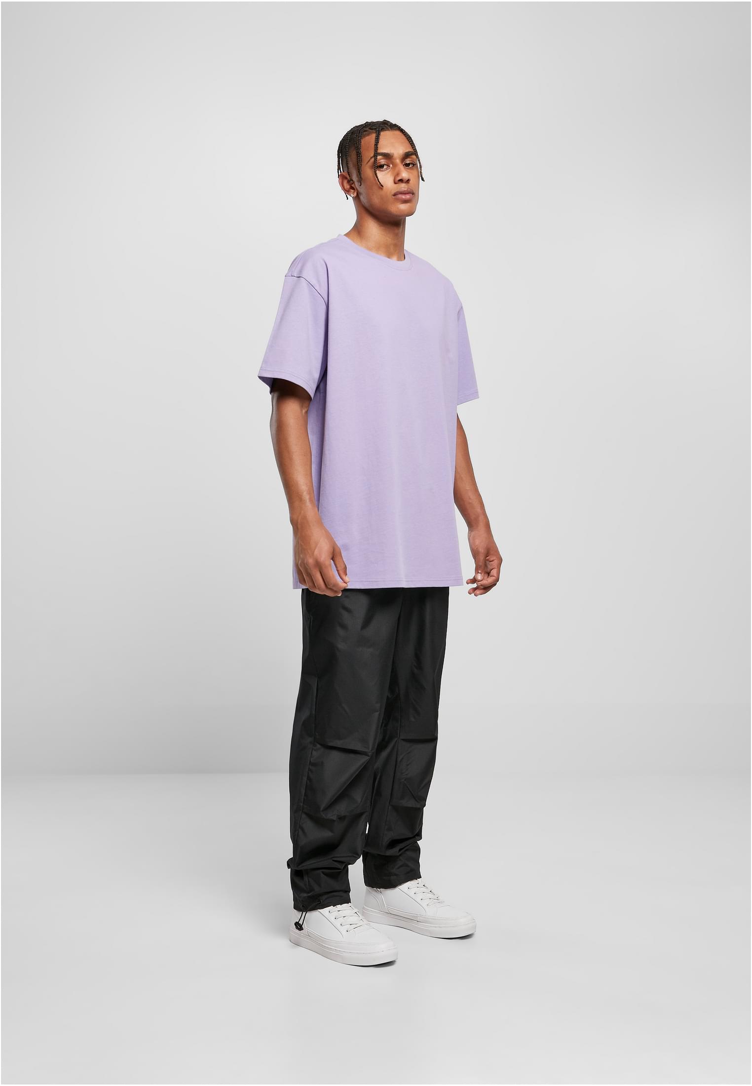 Manlig modell i en ljuslila UC Heavy Oversized Tee, svarta byxor och vita sneakers.
