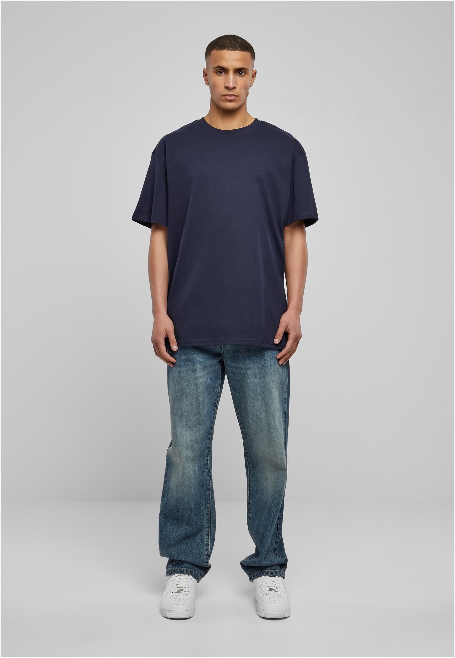 Helkroppsbild framifrån av en man som bär en mörkblå oversized t-shirt, blåa jeans och vita sneakers.