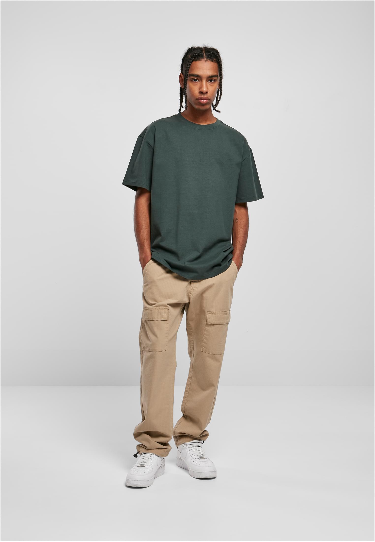 Manlig modell som bär en mörkgrön Heavy Oversized Tee, beiga cargobyxor och vita sneakers.