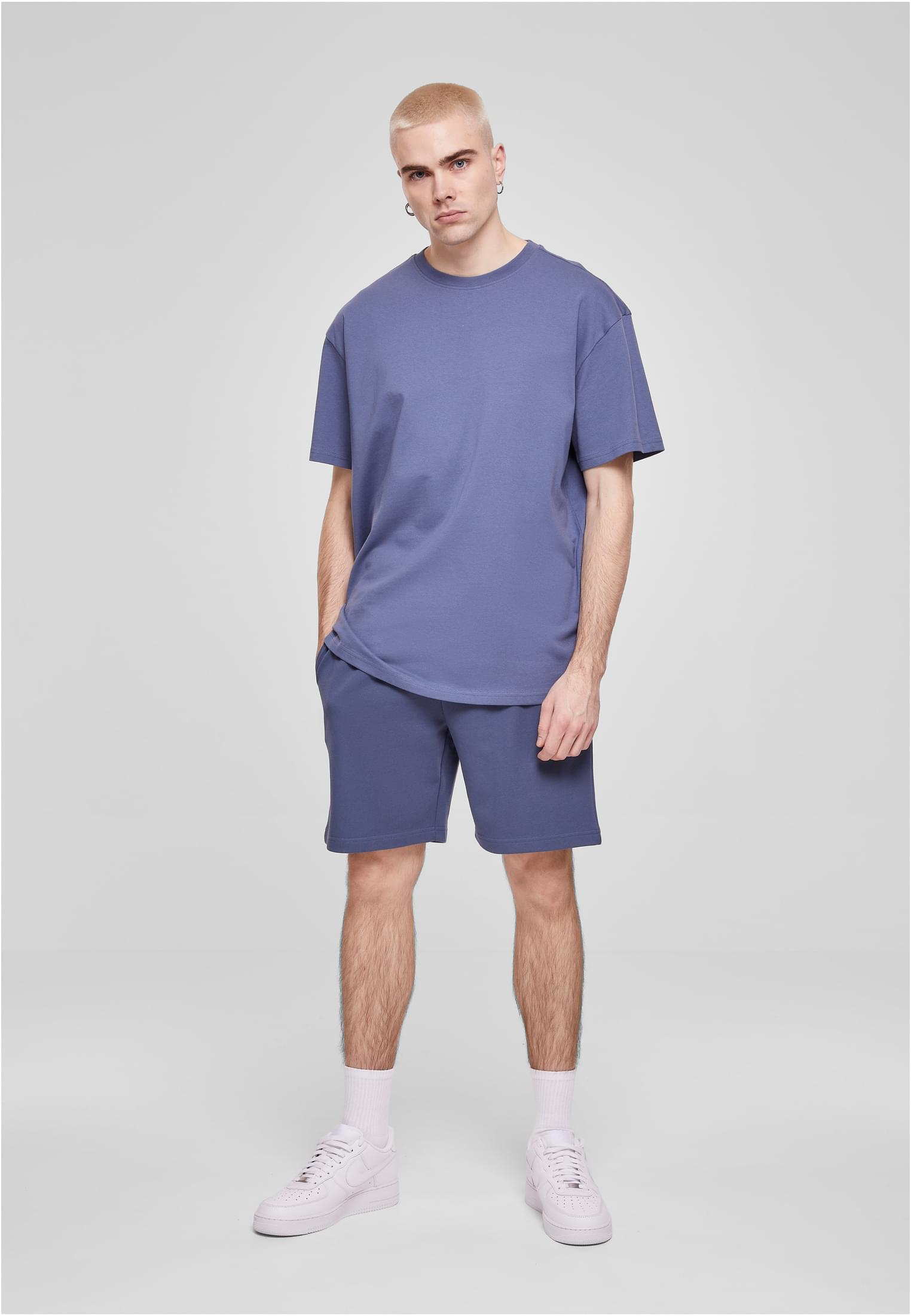 En manlig modell poserar i en oversized, dovblå t-shirt och matchande shorts mot en ljusgrå bakgrund.