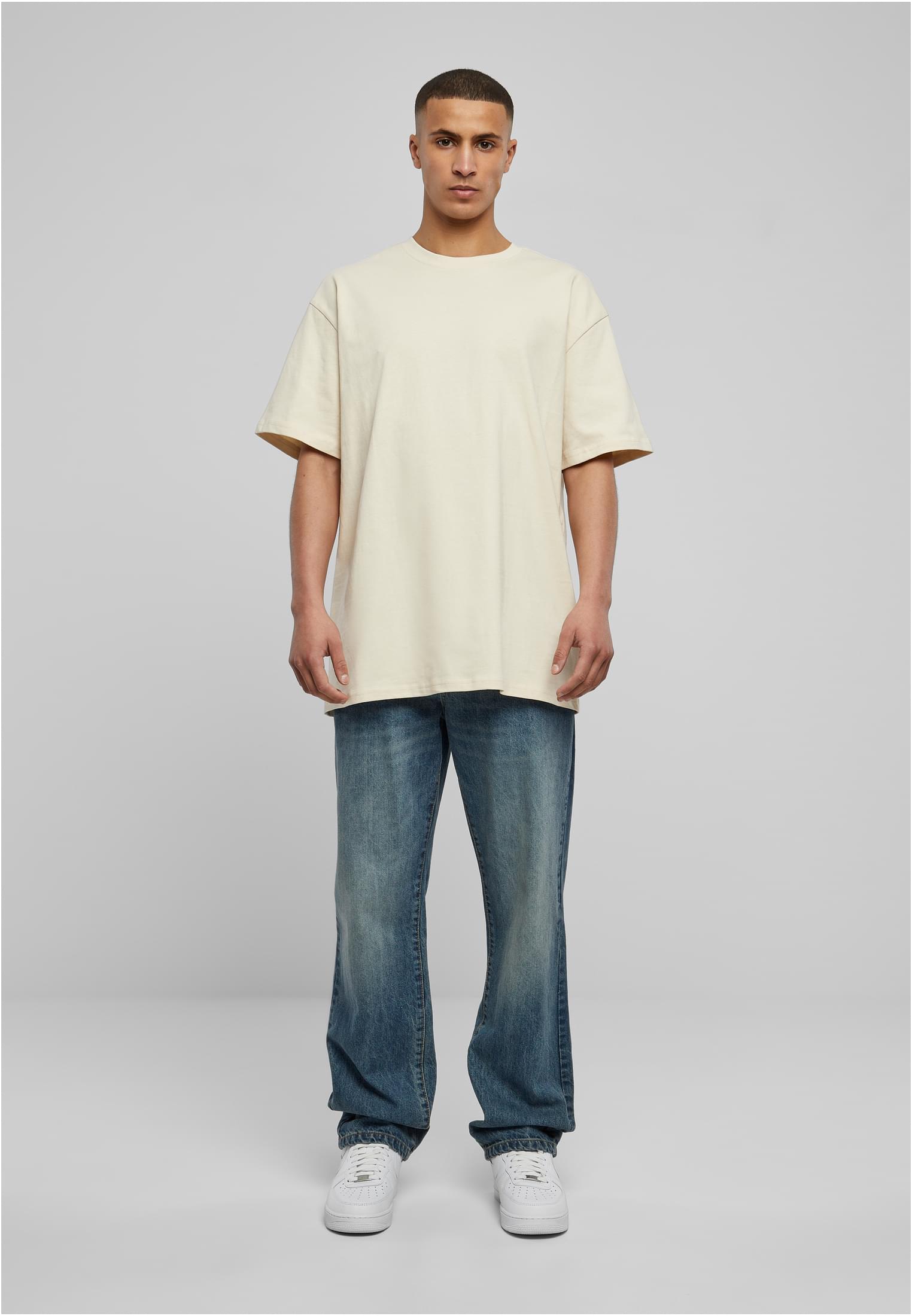 Helkroppsbild av en man som bär en ljus Heavy Oversized Tee, blå jeans och vita sneakers.
