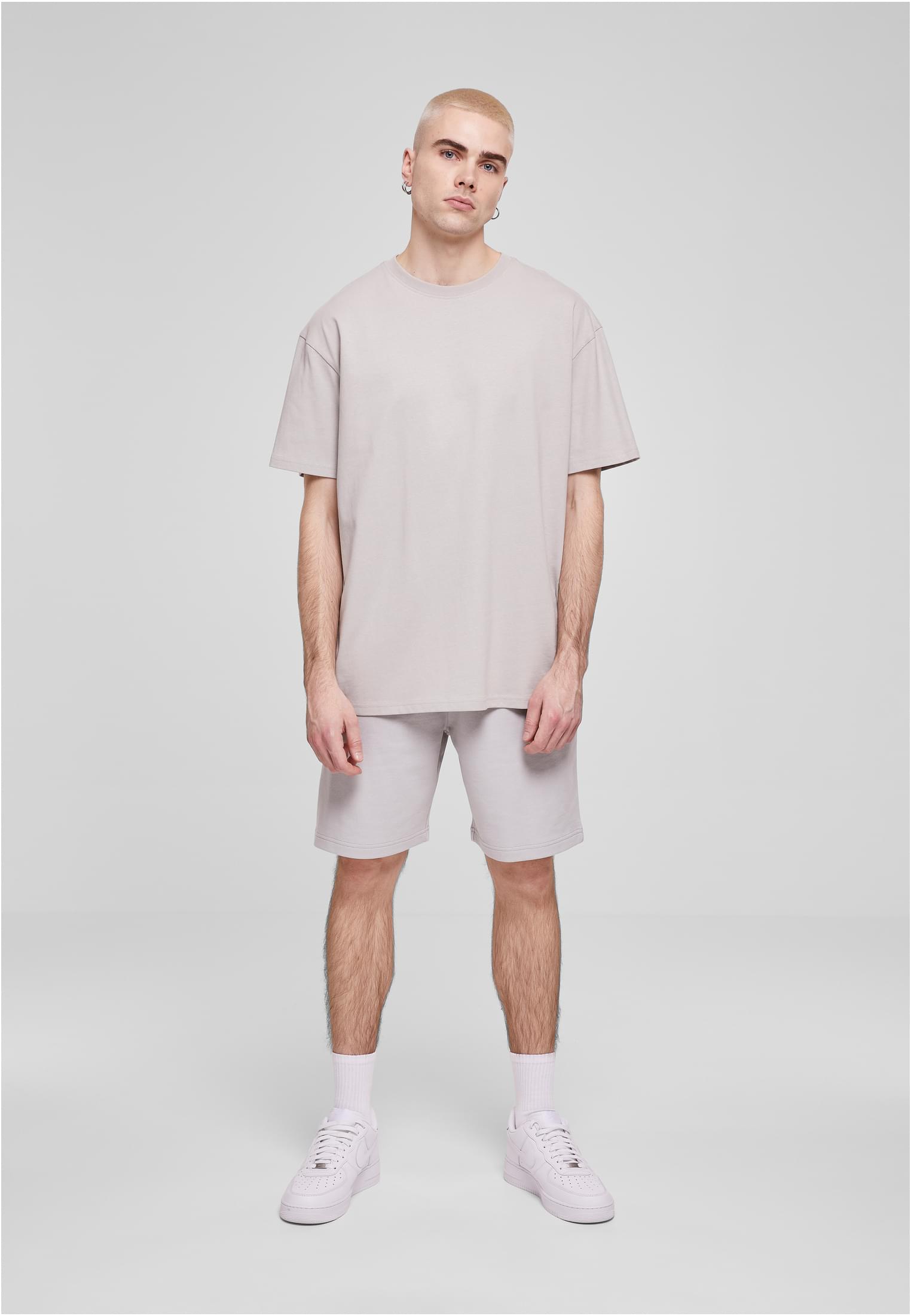 En manlig modell sedd framifrån, klädd i en ljusgrå oversized t-shirt och matchande shorts.