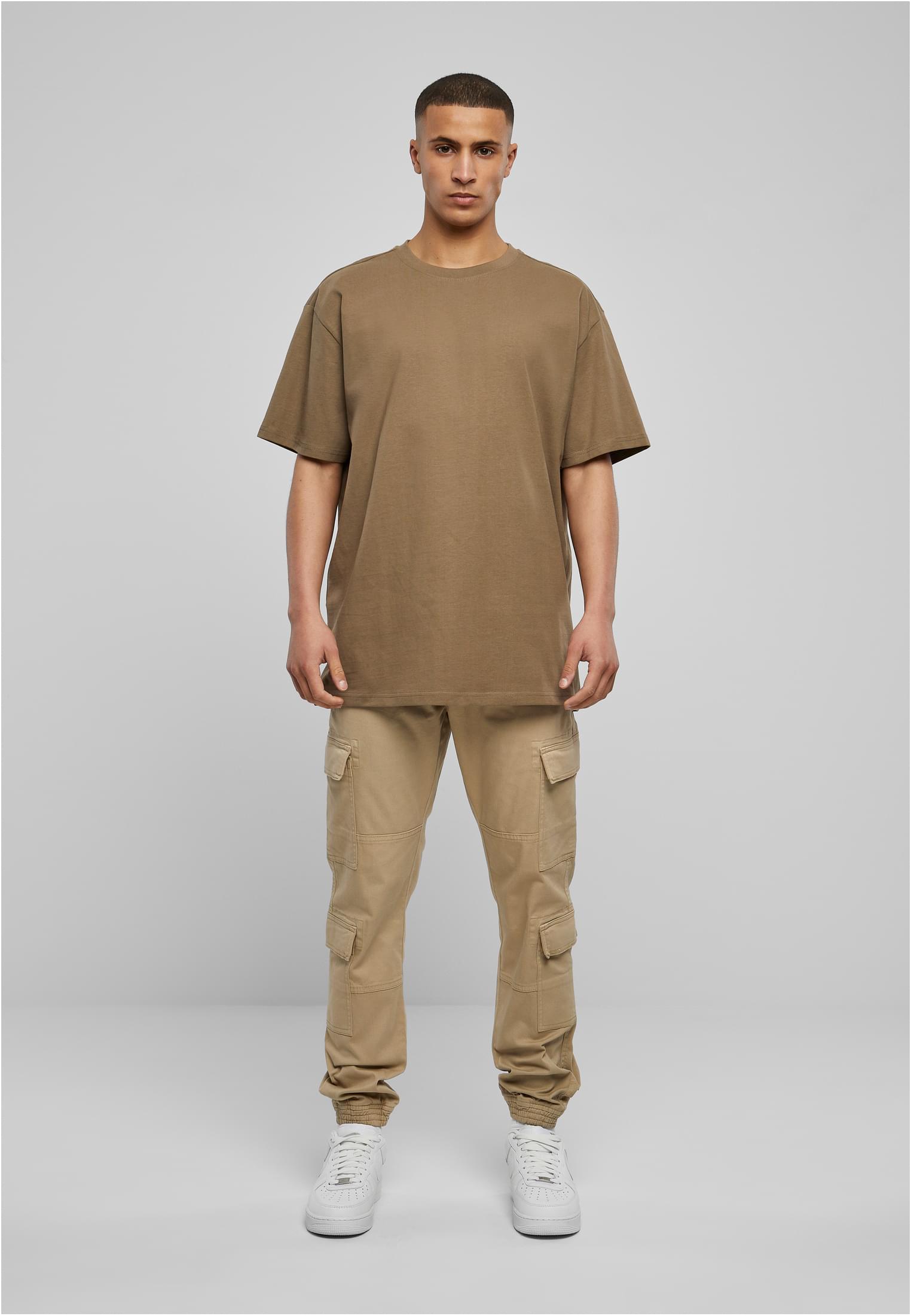 Manlig modell sedd framifrån i en brun oversized t-shirt, beiga cargobyxor och vita sneakers.