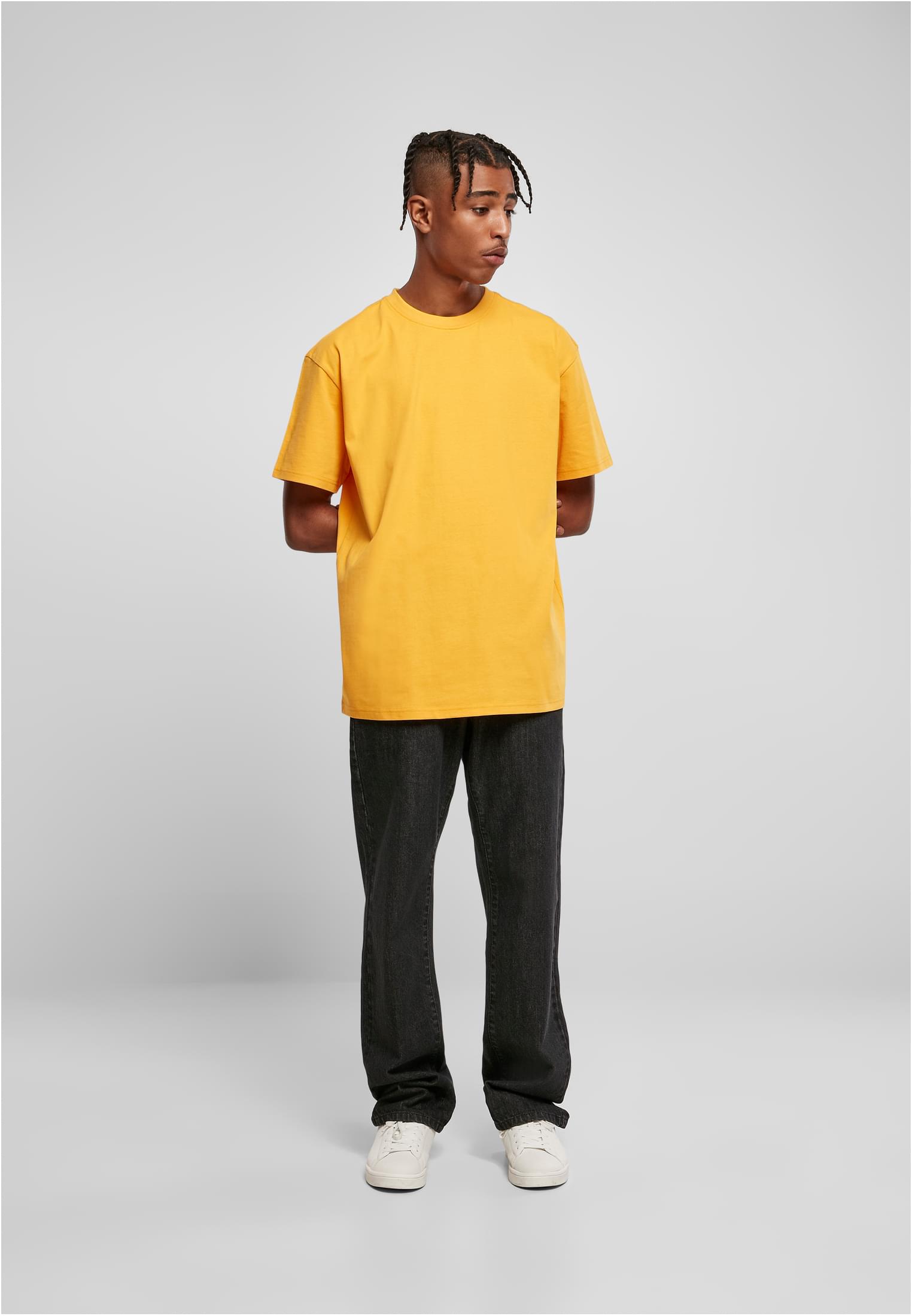 En man som bär en gul Heavy Oversized Tee från Urban Classics, mörka jeans och vita skor.