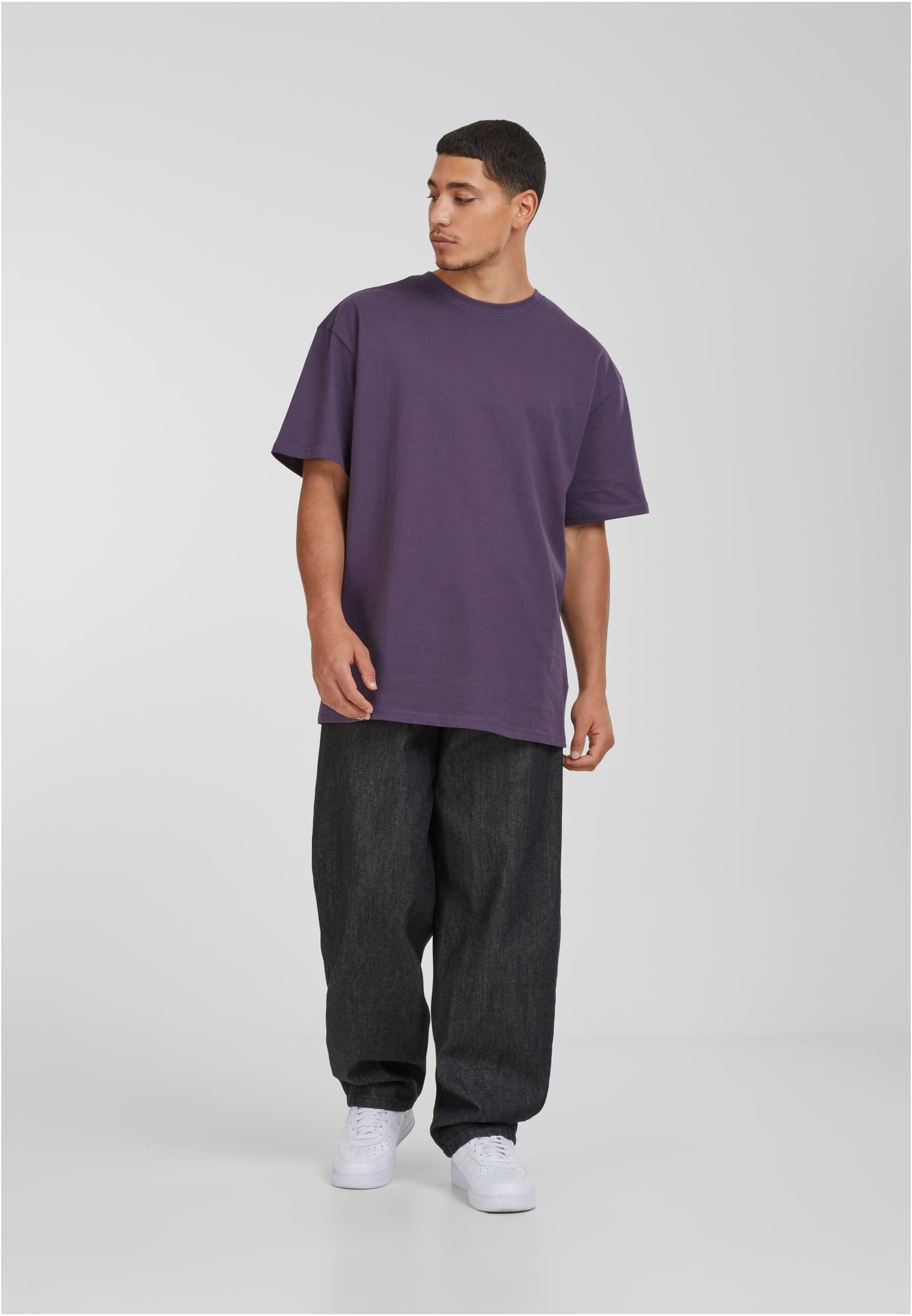 Manlig modell i lila Urban Classics Heavy Oversized Tee, svarta jeans och vita sneakers.