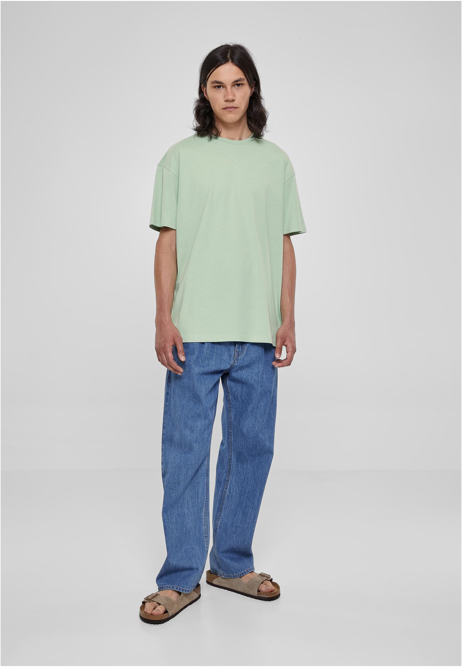 En man bär en Heavy Oversized Tee i mintgrön färg, tillsammans med blåa jeans.