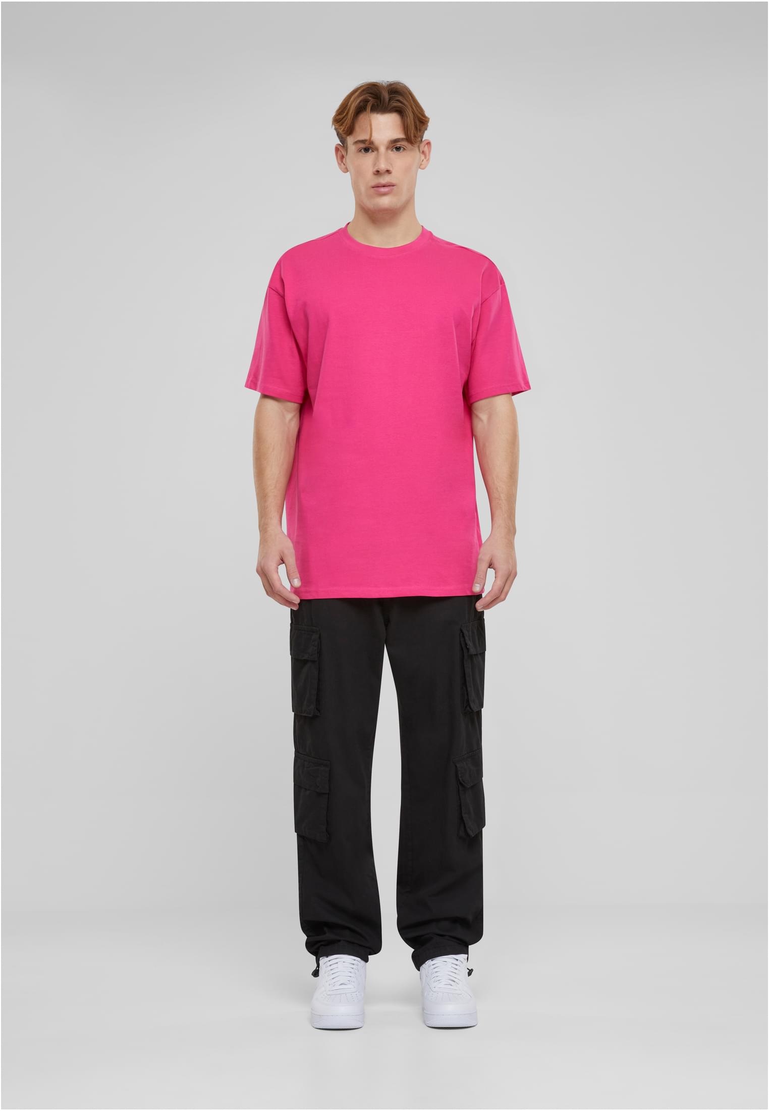 En man poserar i en rosa oversized t-shirt, svarta cargobyxor och vita sneakers.
