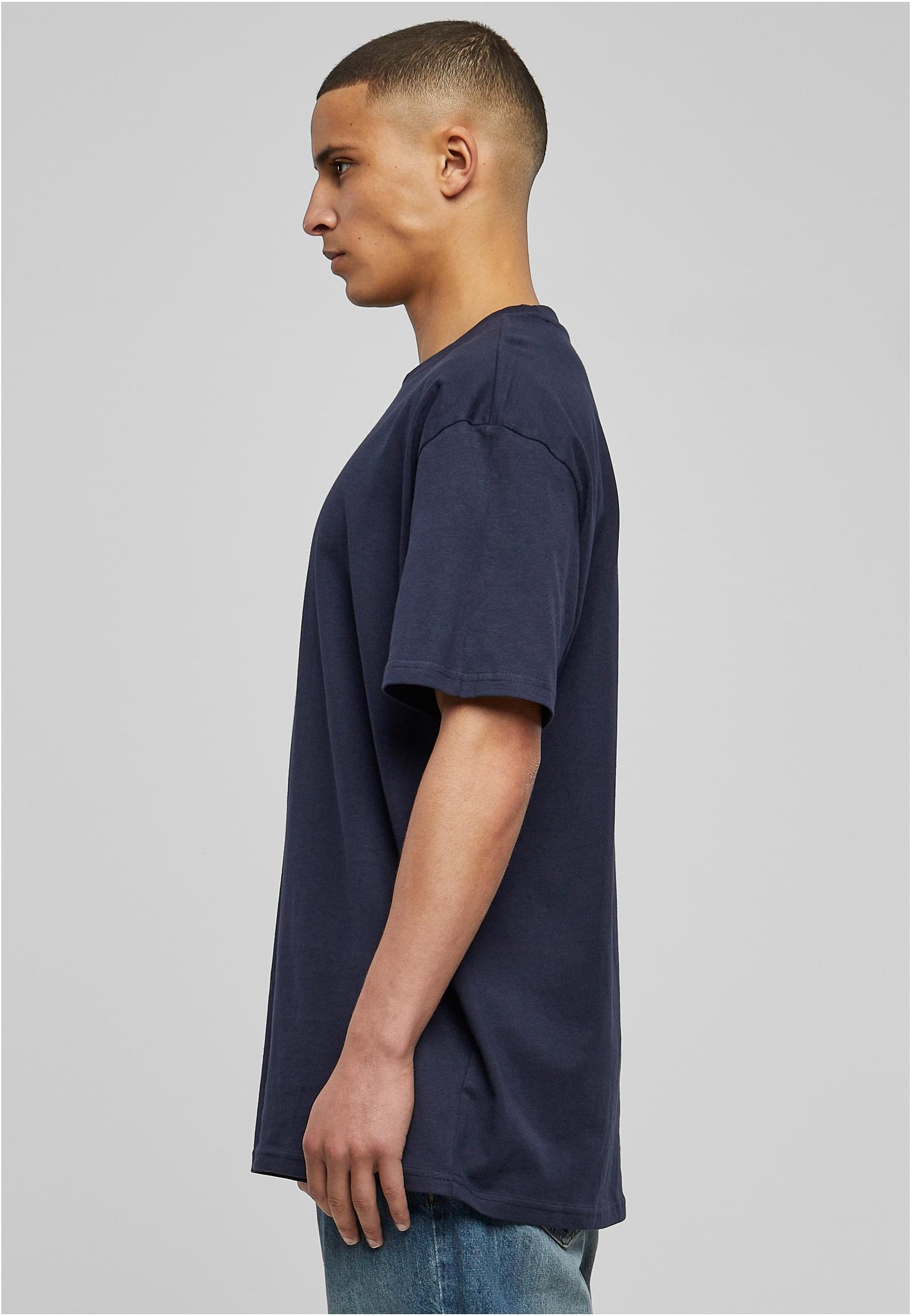 En man sedd från sidan som bär en mörkblå oversized t-shirt och jeans mot en ljusgrå bakgrund.
