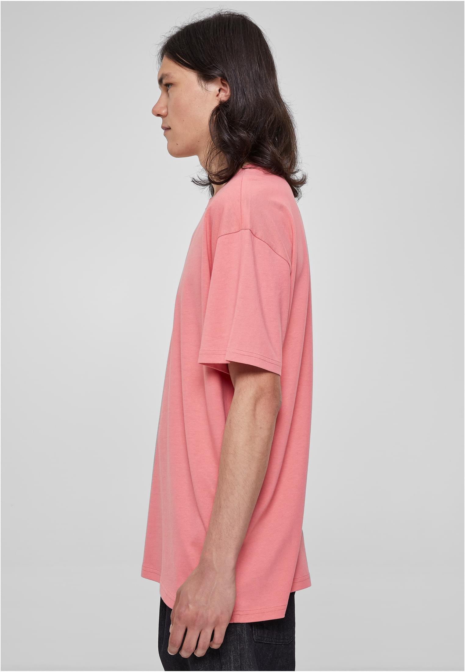 Man med långt hår i profil, bärandes en ljusrosa oversized t-shirt.