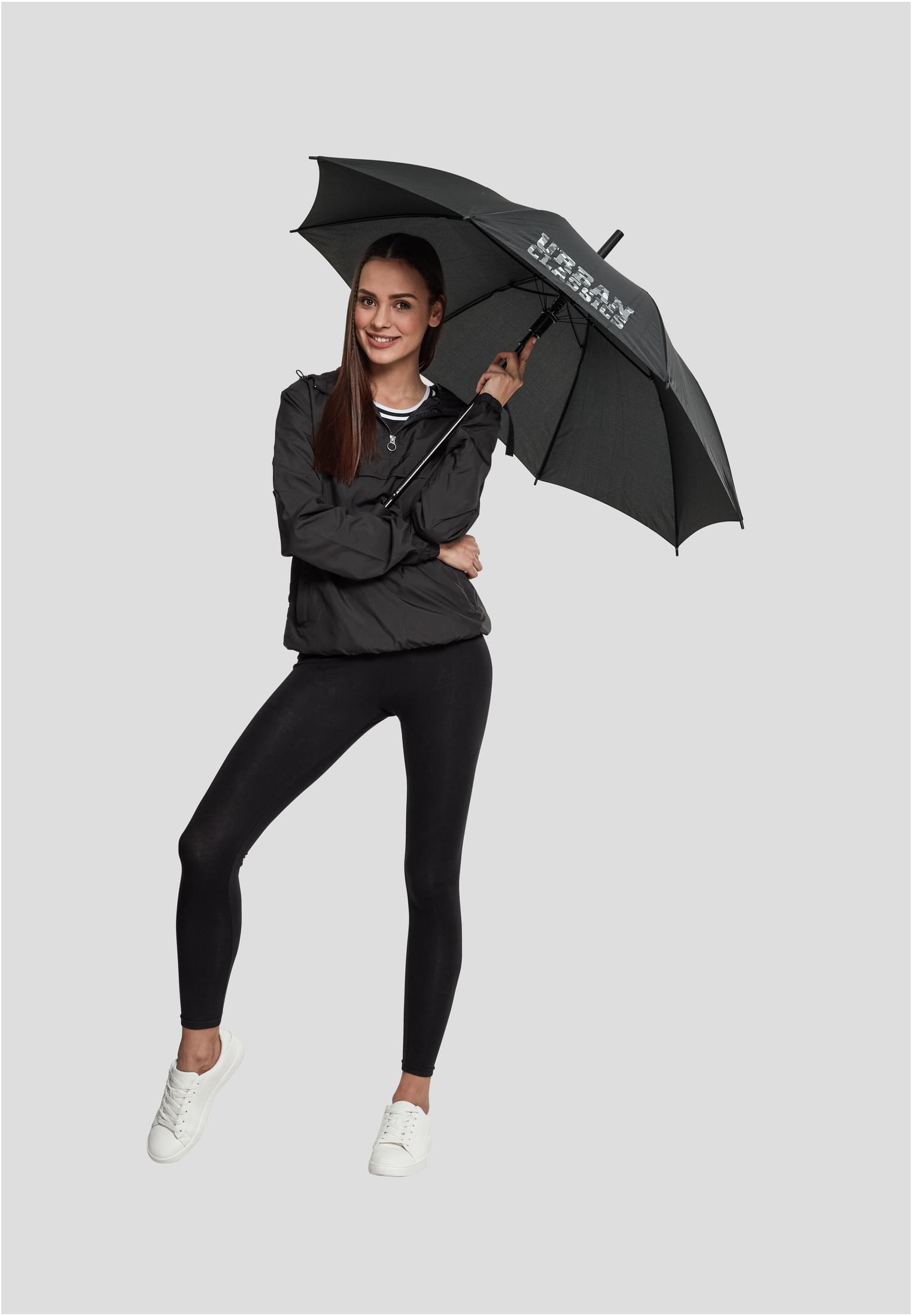 En kvinna som poserar i en svart Dam Basic Pull Over Jacka, svarta leggings och vita sneakers, medan hon håller i ett svart paraply från Urban Classics.