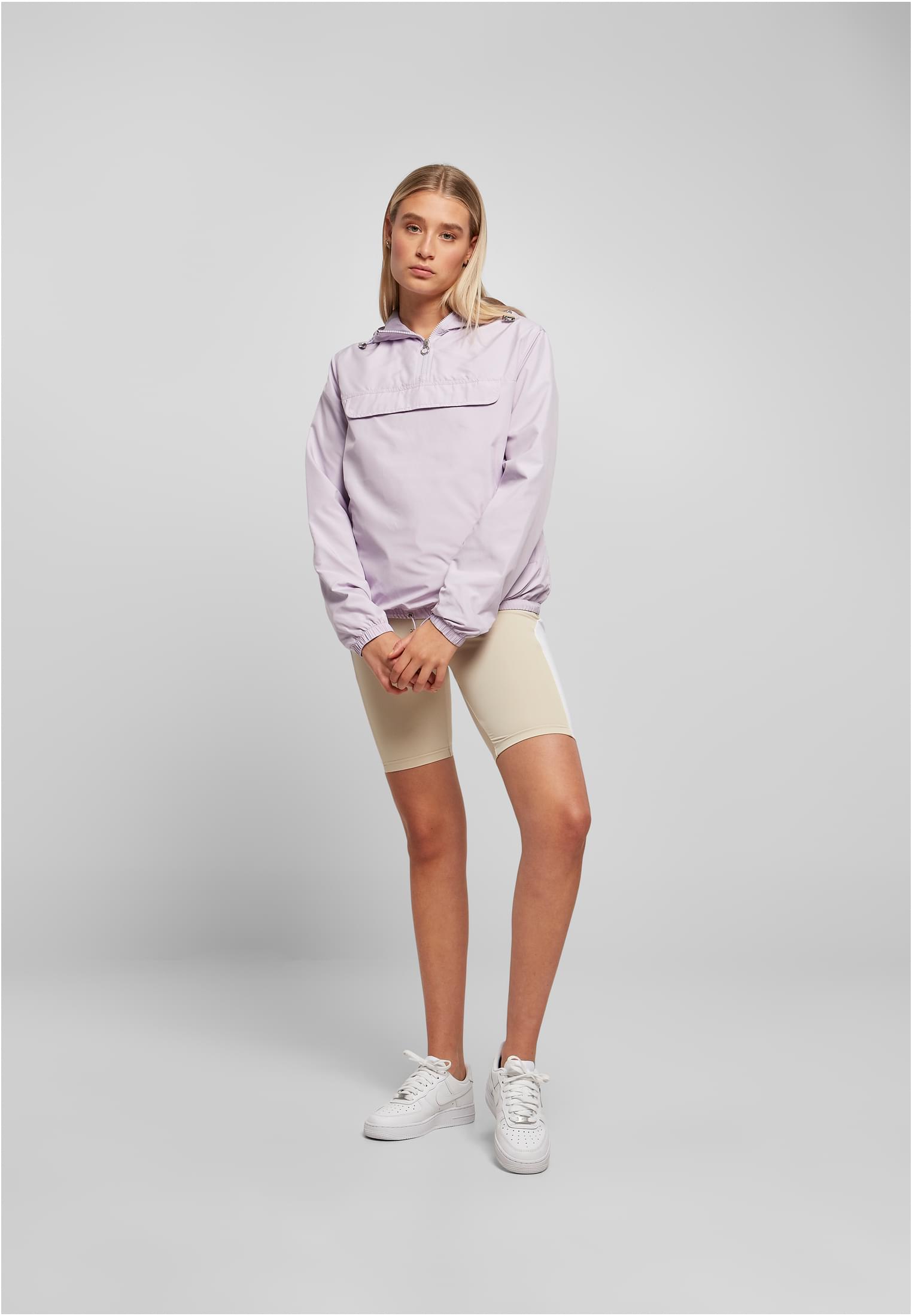 En kvinna som bär en ljuslila pulloverjacka, beiga cykelbyxor och vita sneakers.