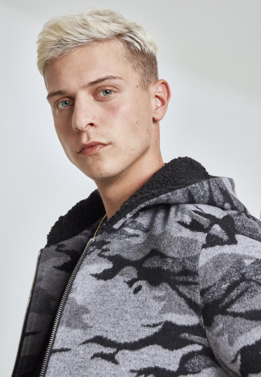 Närbild på en man som bär den grå kamouflagemönstrade jackan UC Camo Zip Jacket, som har en svart sherpafodrad huva.