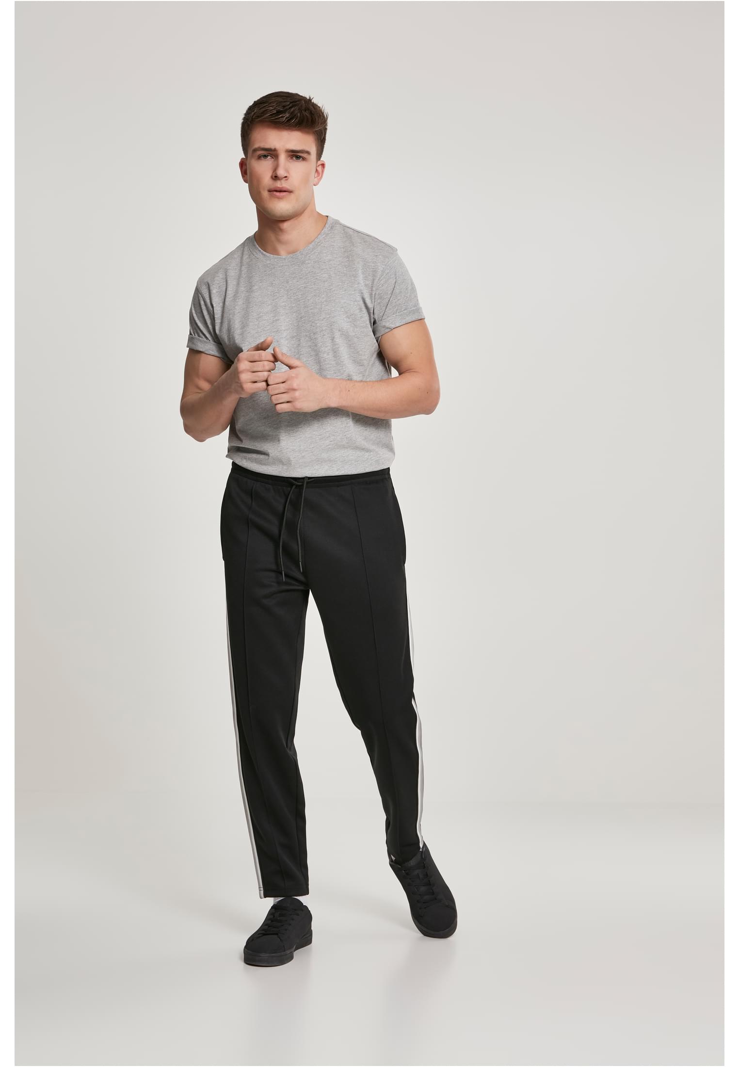 En man som bär en grå t-shirt och svarta träningsbyxor med vita ränder.