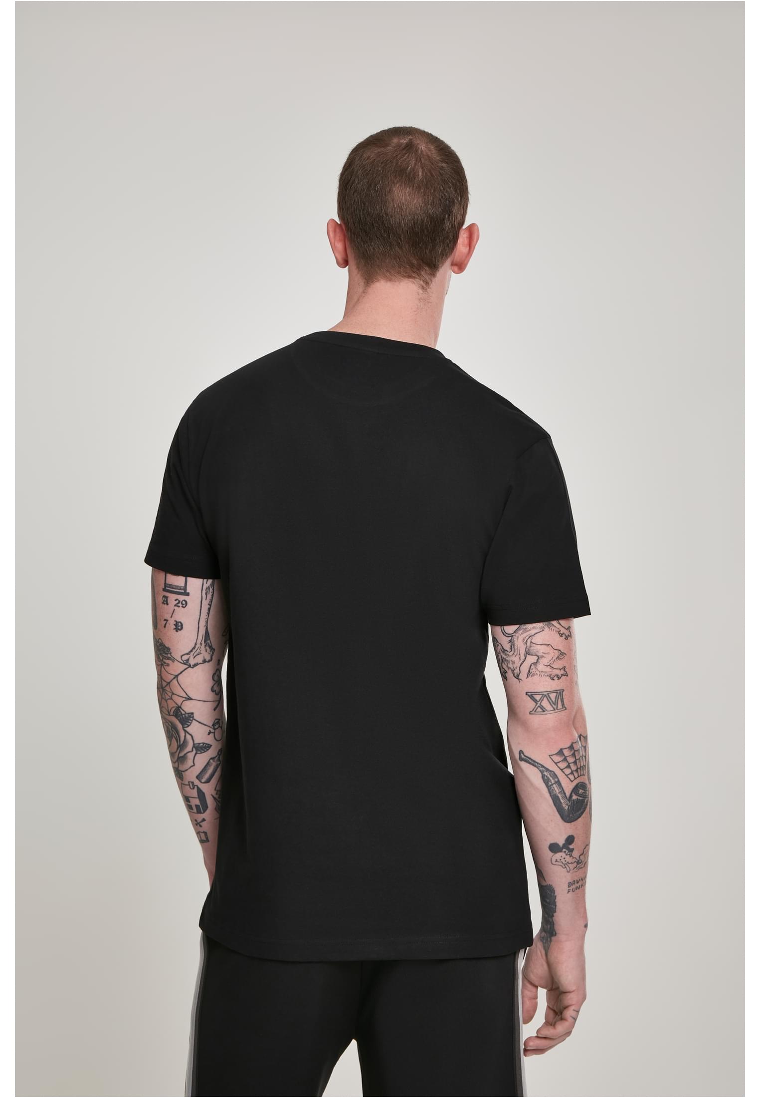 En man med tatueringar visar baksidan av en svart t-shirt.