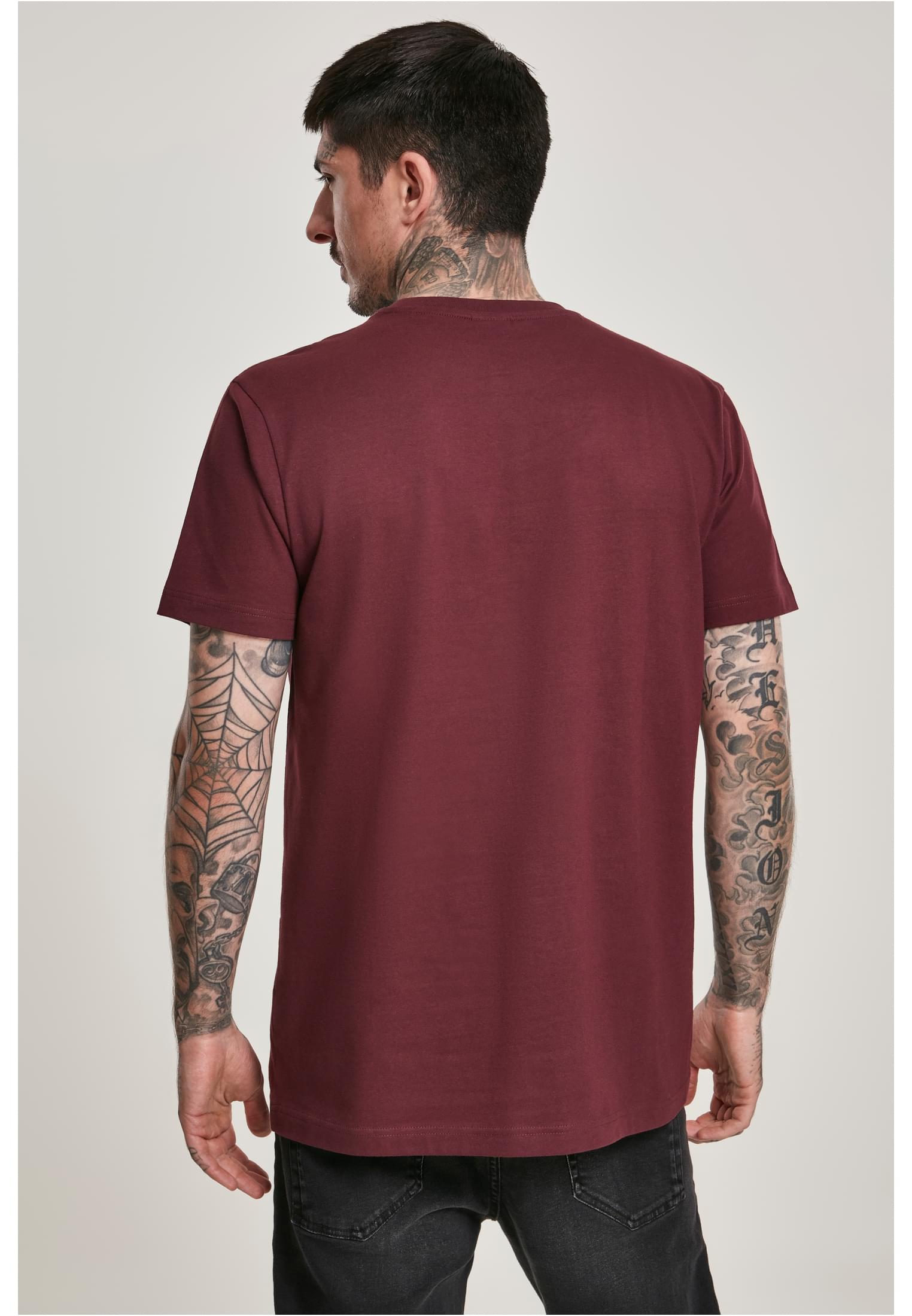 En man med tatueringar visar baksidan av en vinröd t-shirt.