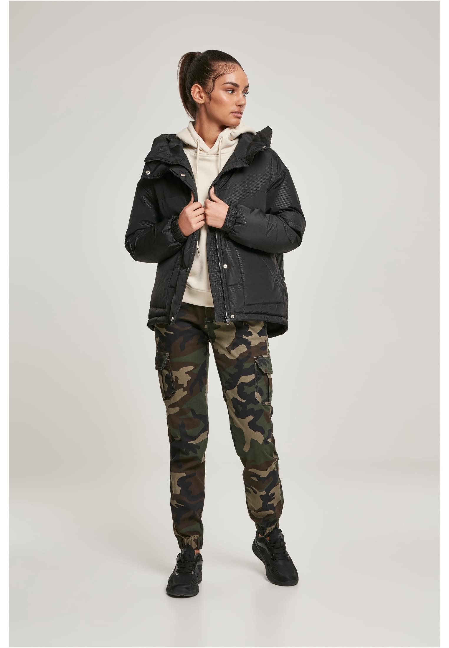 Kvinna som bär en svart pufferjacka, en ljus hoodie, kamouflagemönstrade cargobyxor och svarta sneakers.