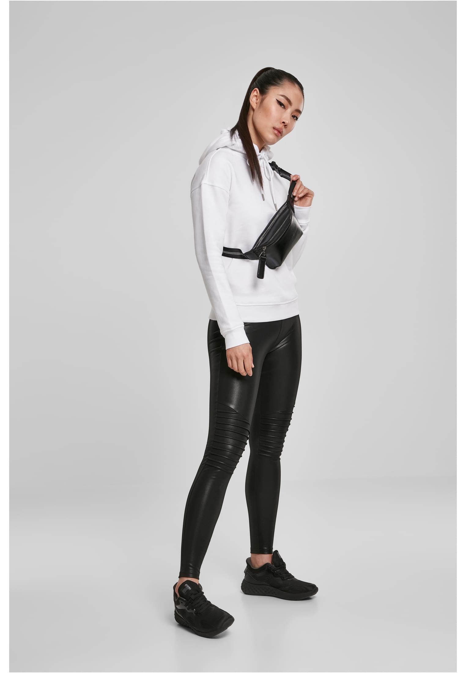 En kvinna som bär en vit luvtröja, svarta leggings i läderimitation och en svart midjeväska.