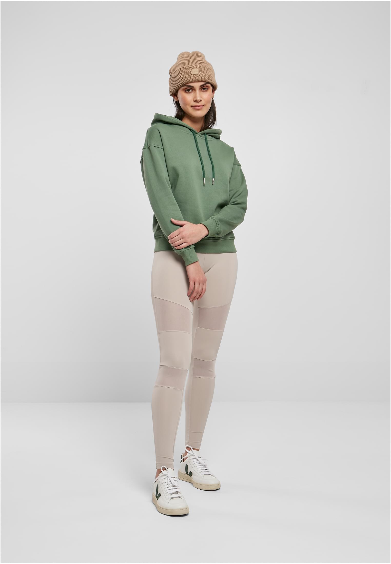 Kvinna som bär den gröna UC Ladies Organic Hoody med beige leggings och mössa.