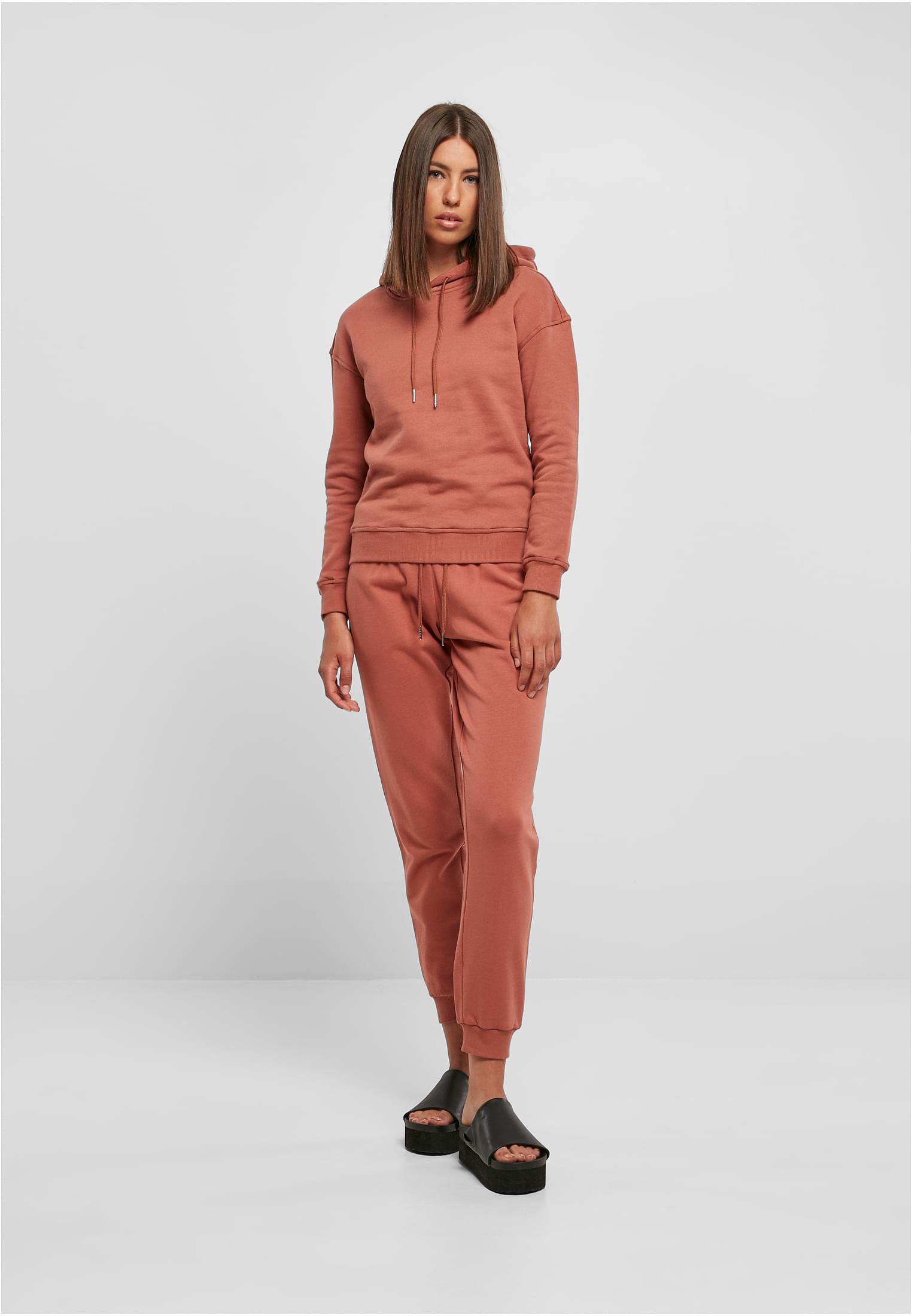 En kvinna som bär en rostbrun UC Ladies Organic Hoody med matchande byxor, fotograferad framifrån mot en ljusgrå bakgrund.