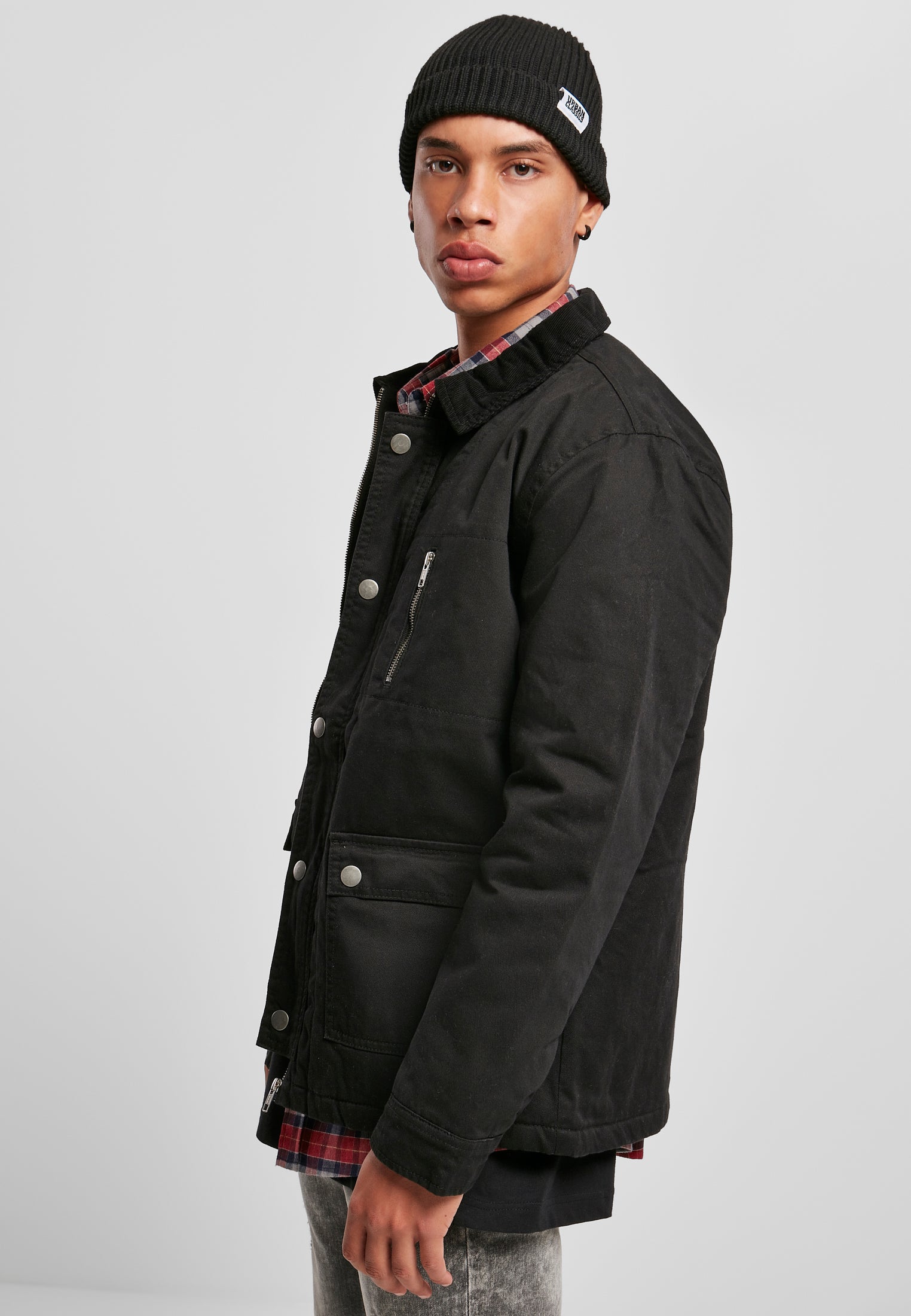 En man med svart mössa visar sidoprofilen av den svarta UC Hunter-jackan.