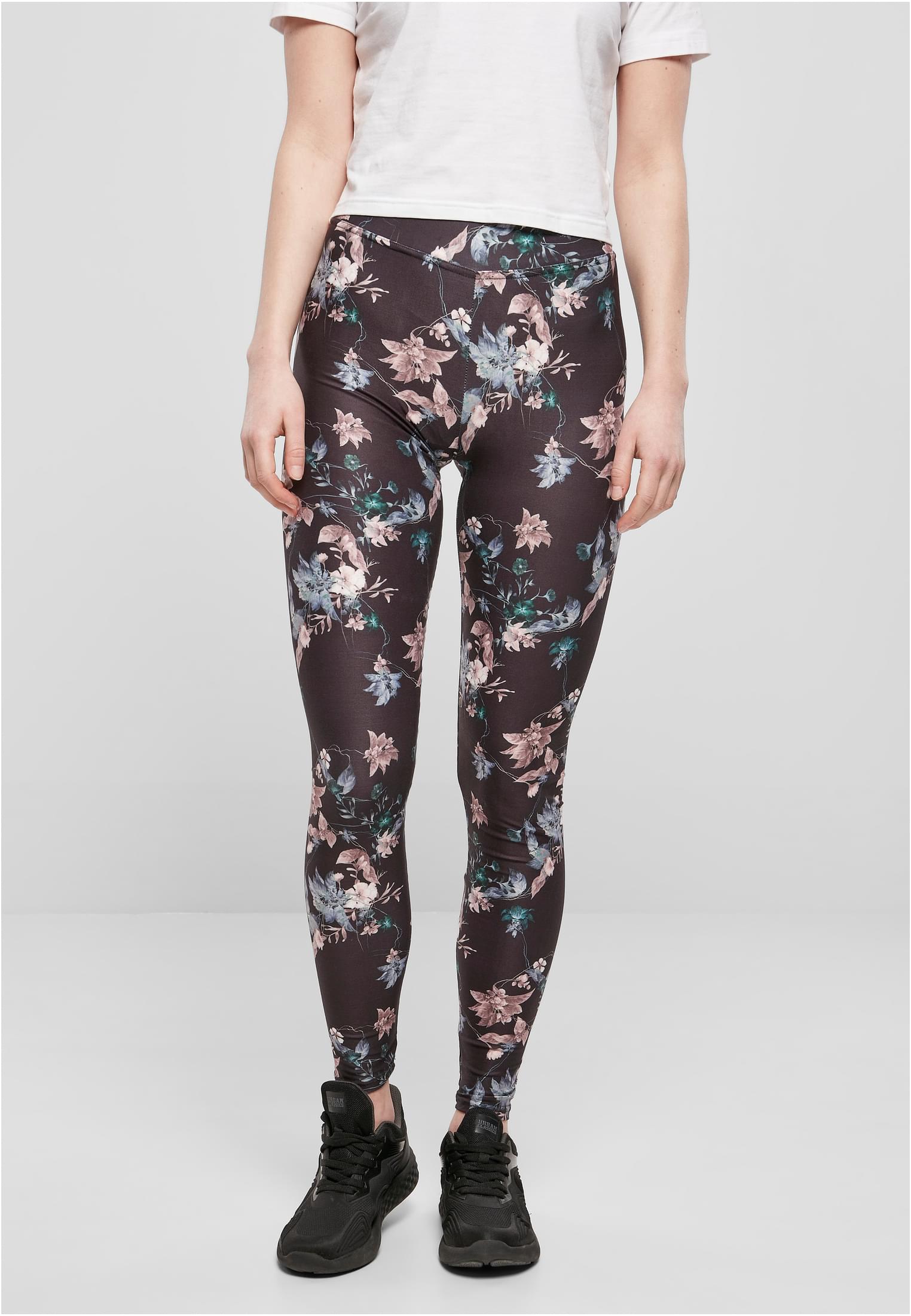 Kvinna sedd framifrån i svarta leggings med blommönster, vit t-shirt och svarta sneakers.