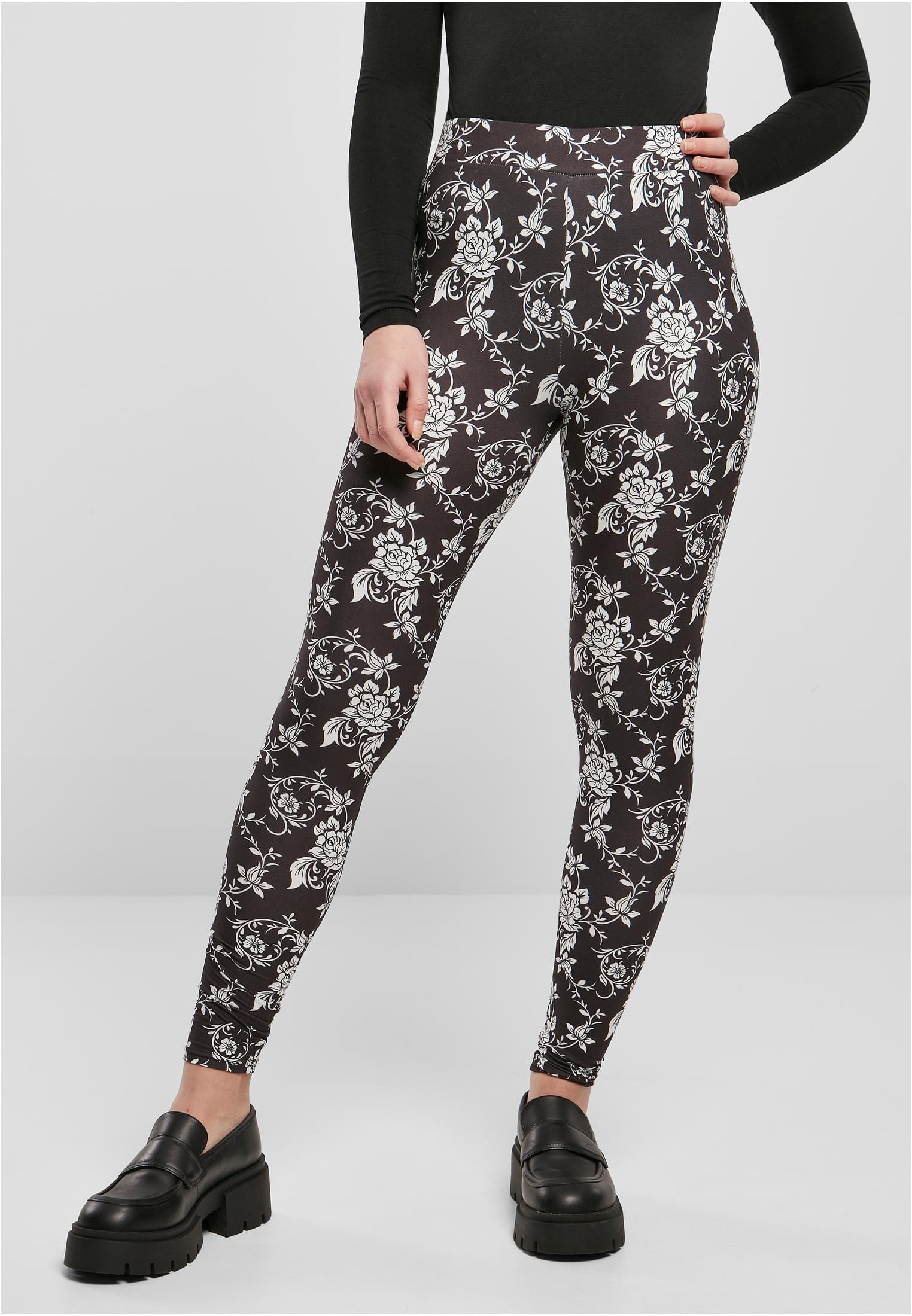 En modell som bär de svarta UC Ladies Soft AOP Leggings med ett heltäckande vitt blommönster, stylade med en svart långärmad tröja och svarta platåskor.