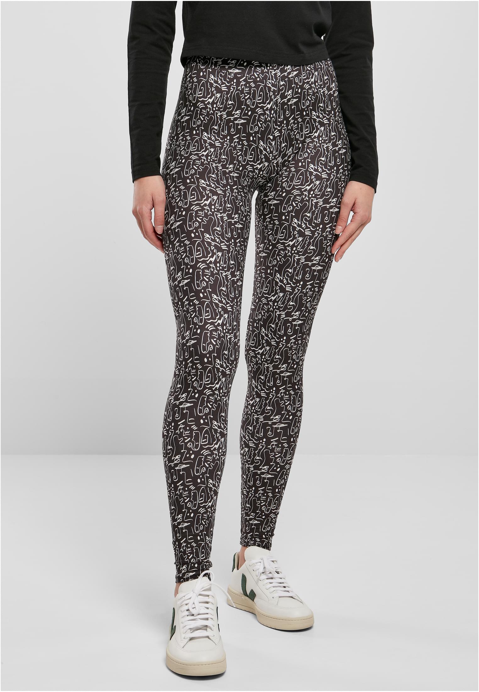 En modell som bär UC Ladies Soft AOP Leggings, som är svarta med ett heltäckande vitt abstrakt mönster. Hon är stylad med en svart långärmad tröja och vita sneakers.