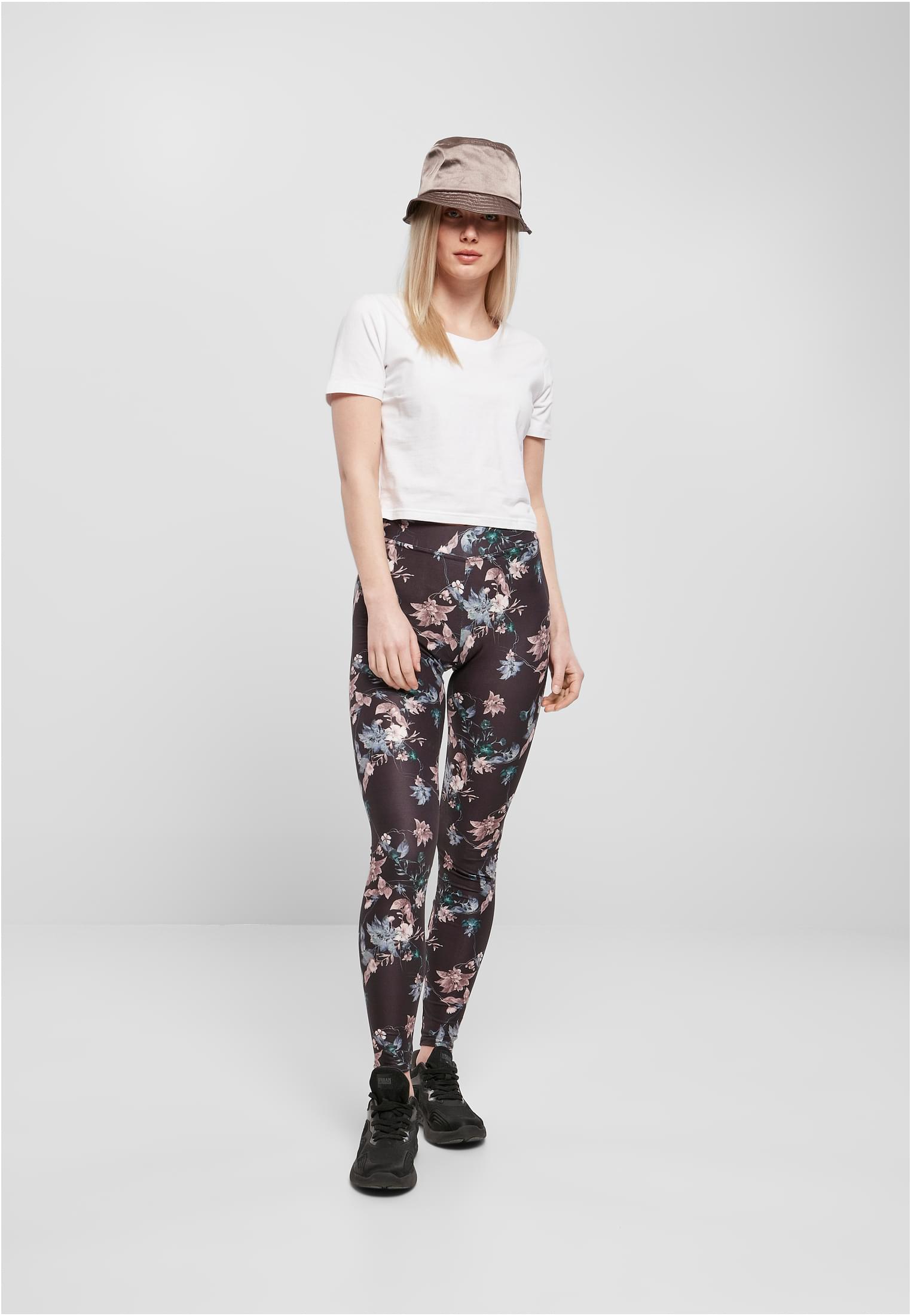 En kvinna som bär svarta leggings med blommigt tryck, en vit t-shirt och en brun hatt.