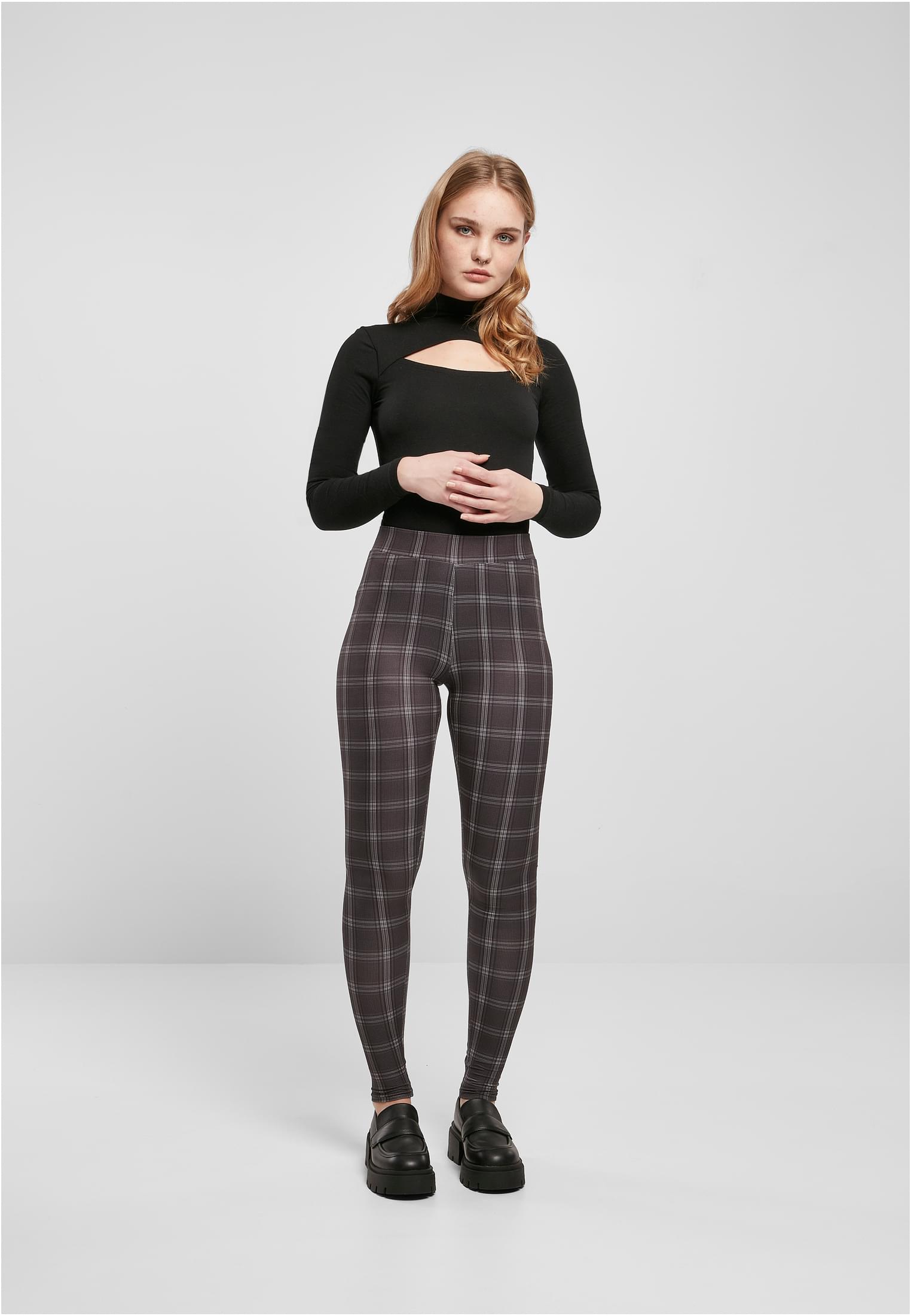 En kvinna som bär de rutmönstrade UC Ladies Soft AOP Leggings, stylade med en svart långärmad topp med utskärning och svarta loafers.