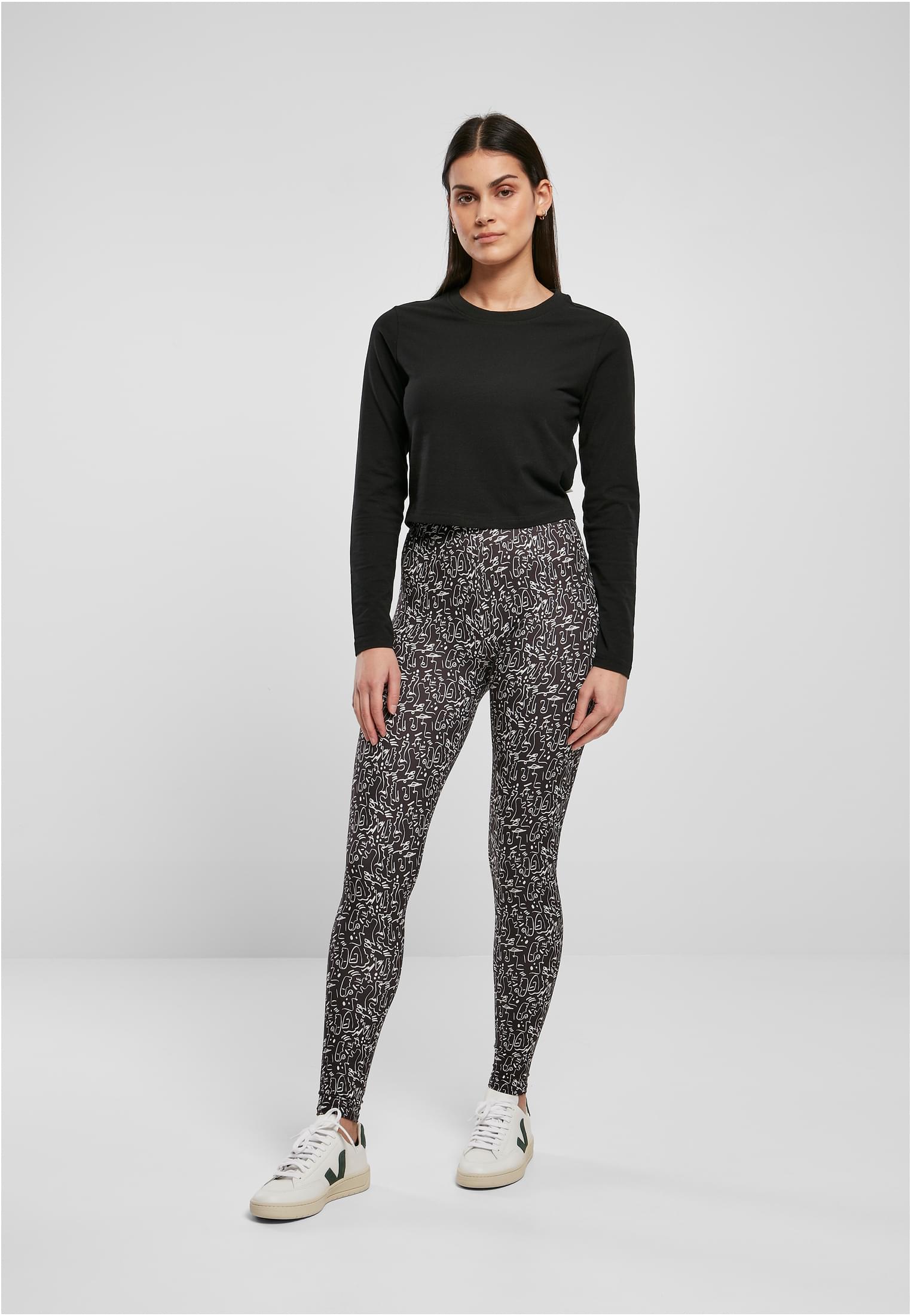 En kvinna som poserar i ett par mönstrade UC Ladies Soft AOP Leggings, stylade med en svart långärmad tröja och vita sneakers mot en ljusgrå bakgrund.