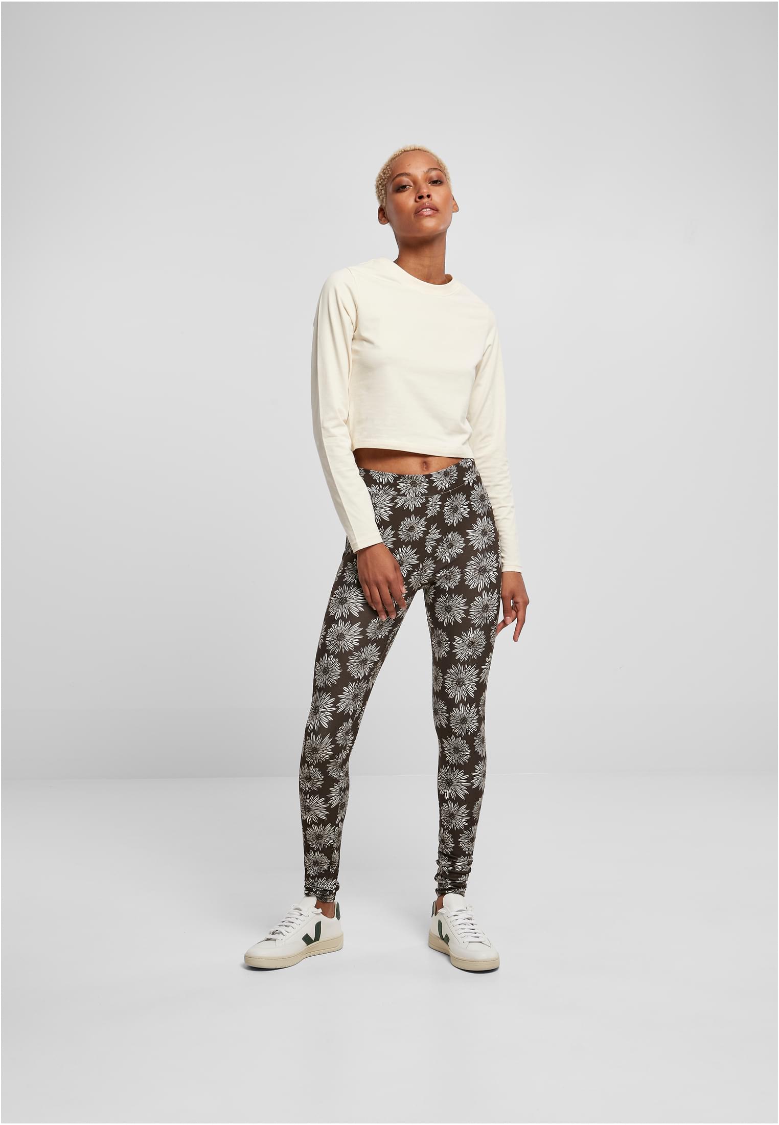 Kvinnlig modell som visar upp UC Ladies Soft AOP Leggings med blommönster, stylade med en krämfärgad långärmad crop top och vita sneakers.