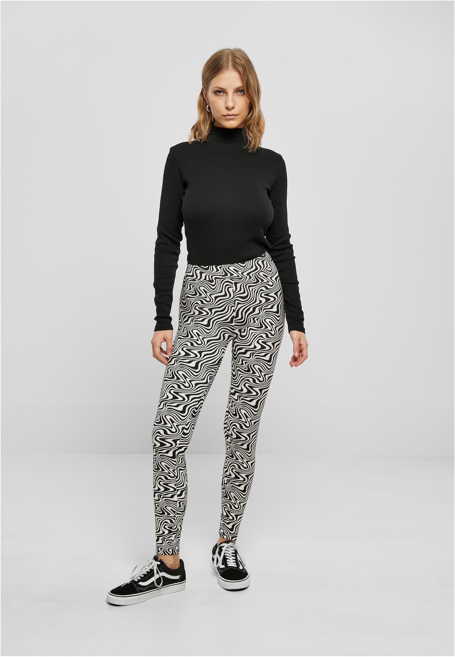 Kvinna som bär svarta och vita mönstrade UC Ladies Soft AOP Leggings tillsammans med en svart polotröja och sneakers.