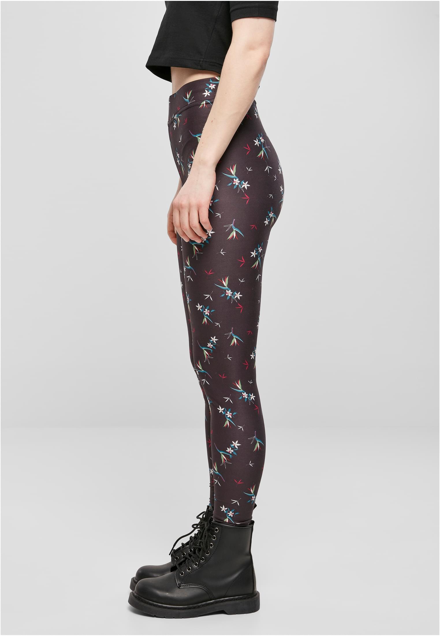 Kvinna sedd från sidan, iklädd svarta leggings med blommönster, en kort svart topp och kängor.