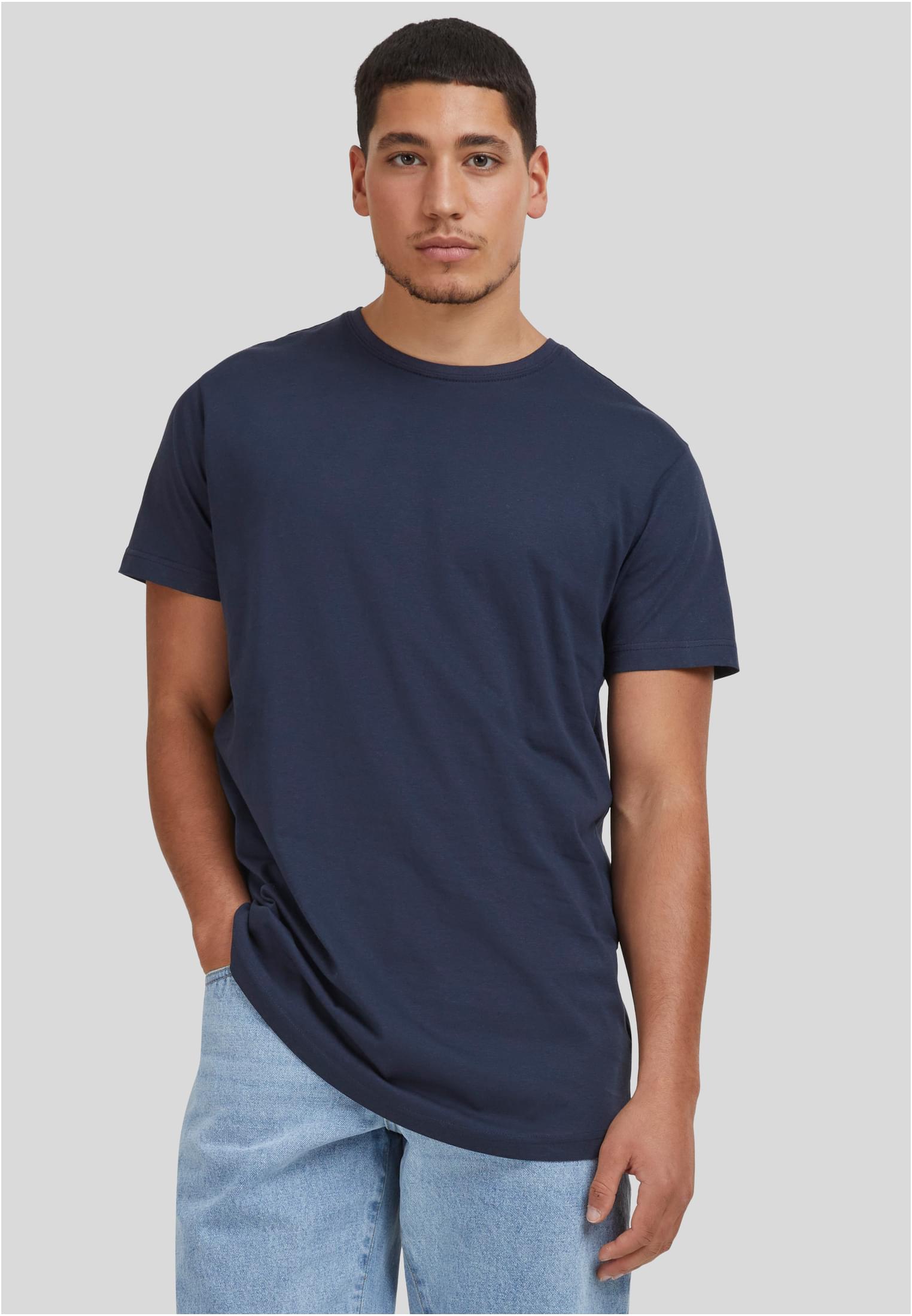 En manlig modell som bär en mörkblå UC Shaped Long Tee och ljusblå jeans, sedd framifrån mot en grå bakgrund.