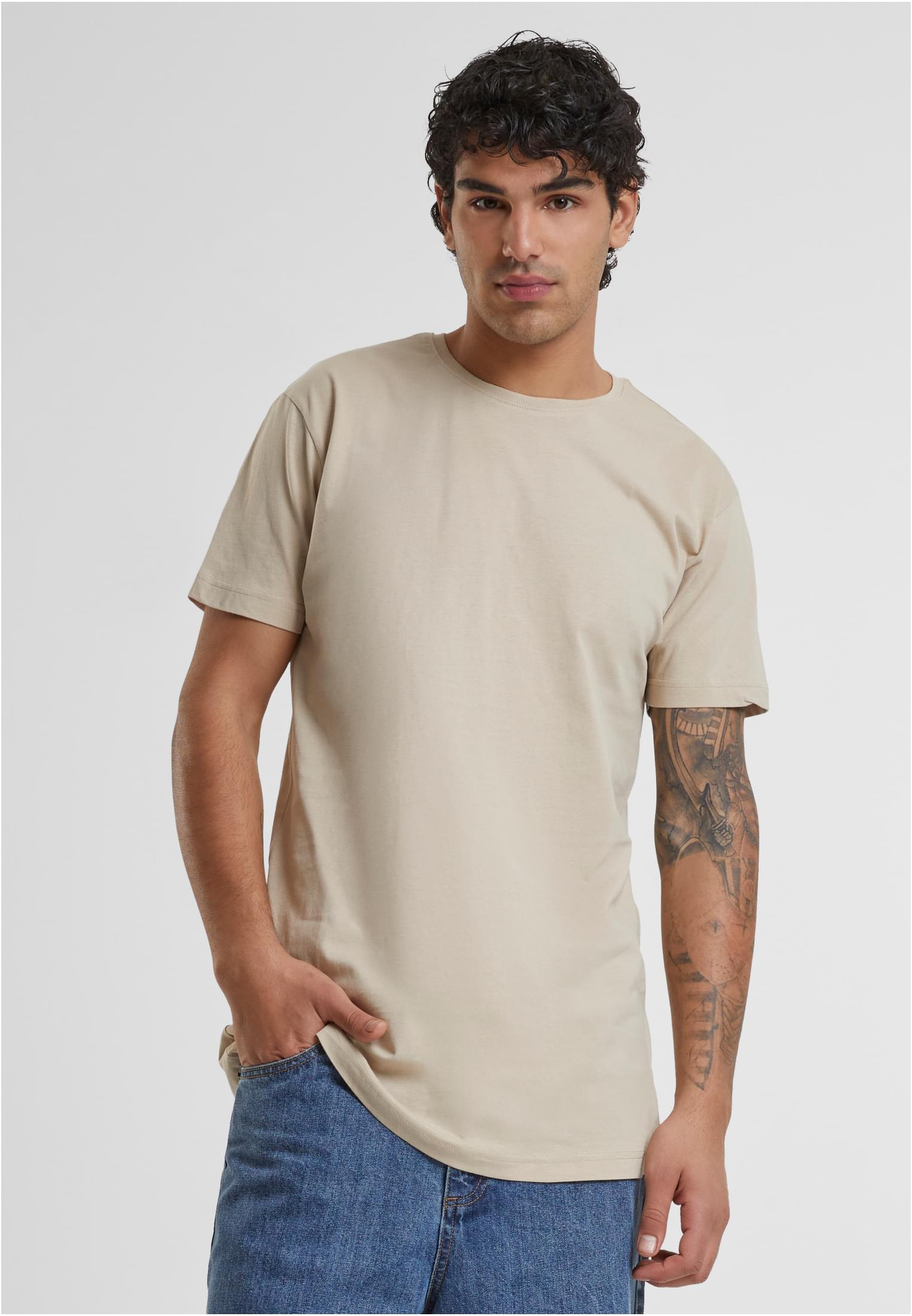 En manlig modell med en tatuering på armen bär en beige, lång t-shirt från Urban Classics.