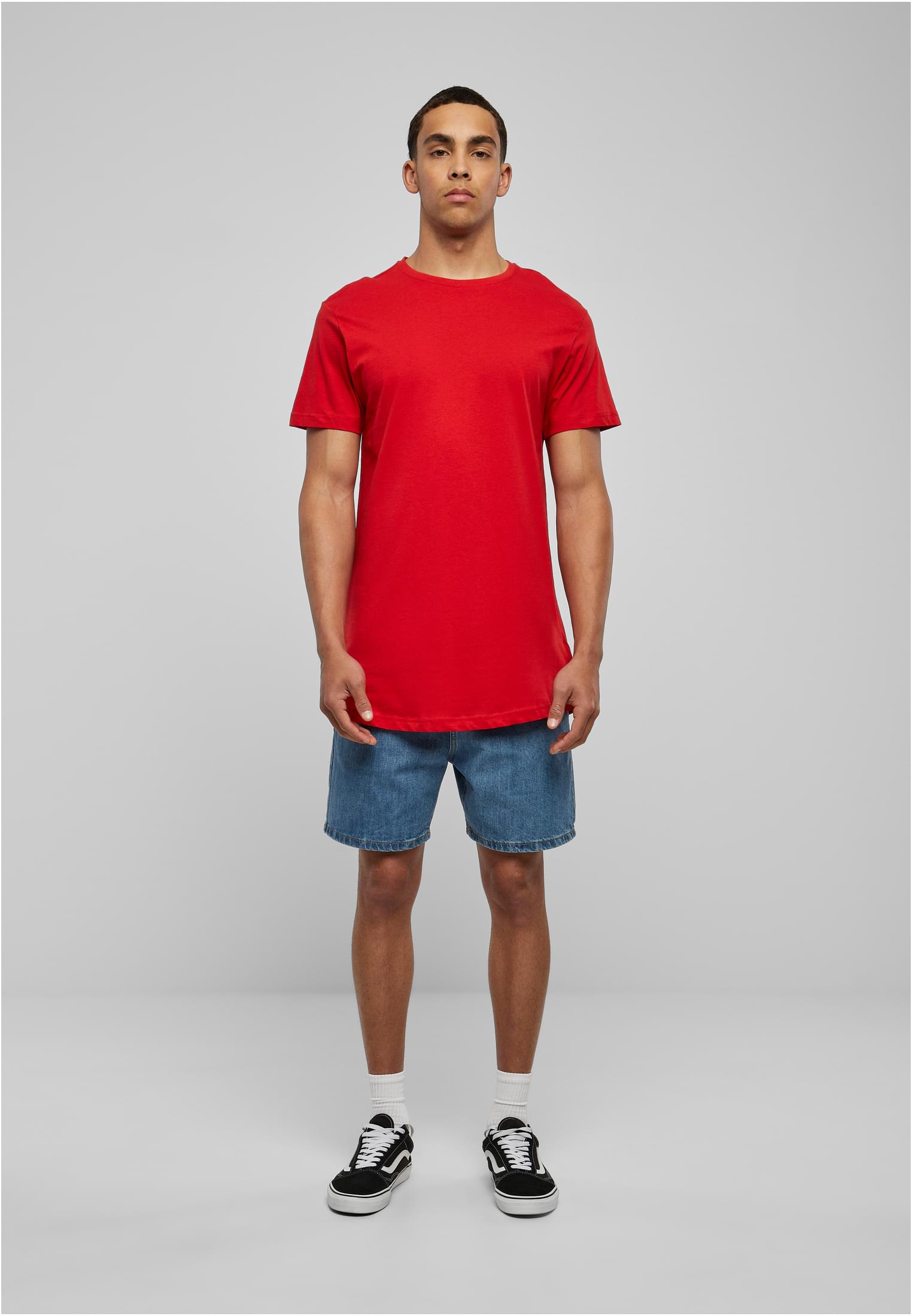 En manlig modell som visar en röd lång t-shirt framifrån, tillsammans med jeansshorts och sneakers.