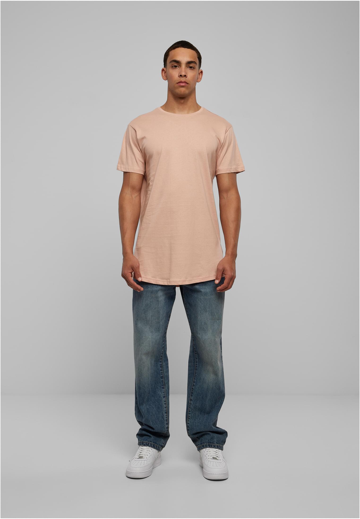 Manlig modell sedd framifrån i en terrakottafärgad Shaped Long Tee, blå jeans och vita sneakers.