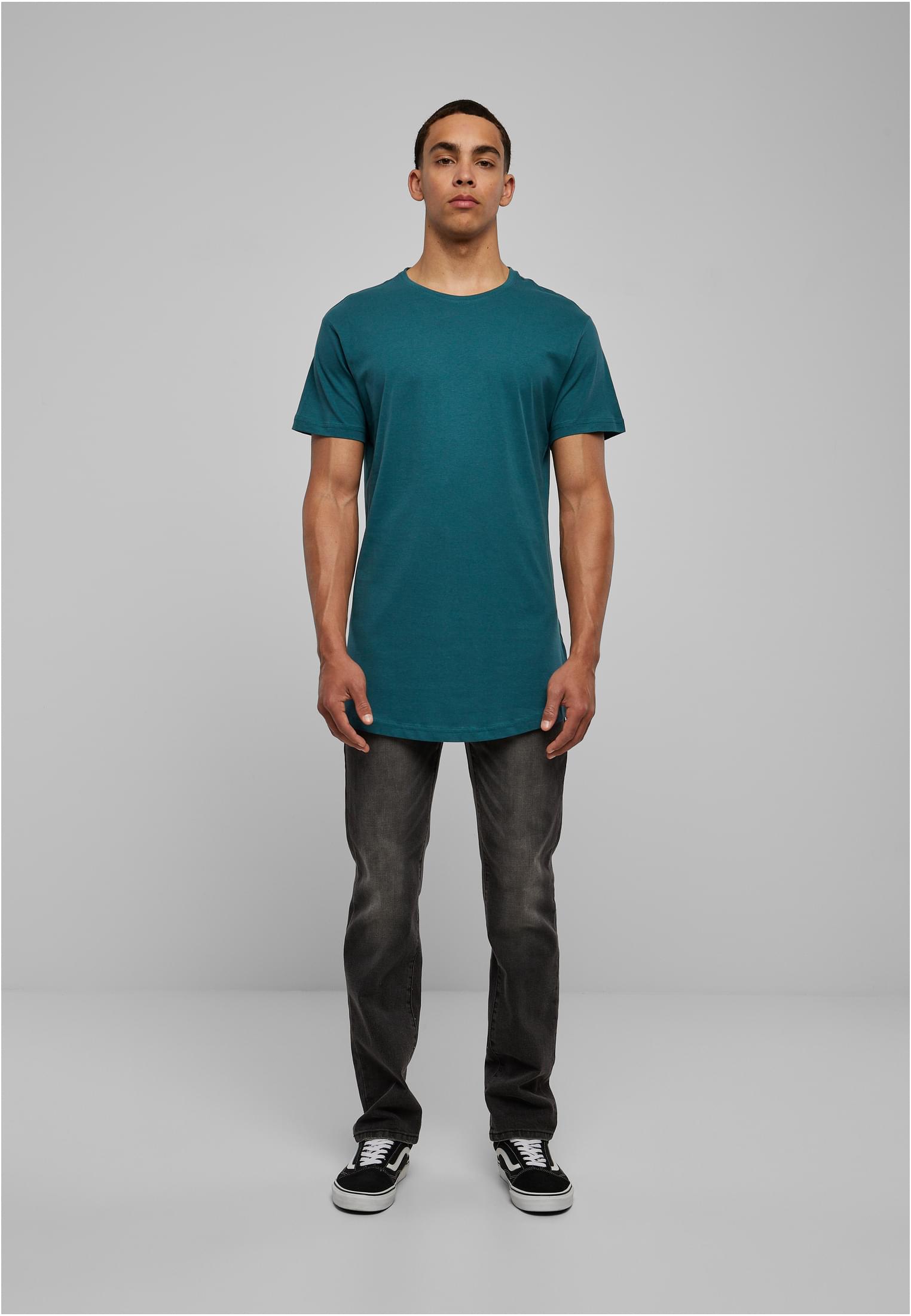 Manlig modell som bär en petrolfärgad UC Shaped Long Tee med mörkgrå jeans och svarta sneakers, fotograferad framifrån mot en ljusgrå bakgrund.